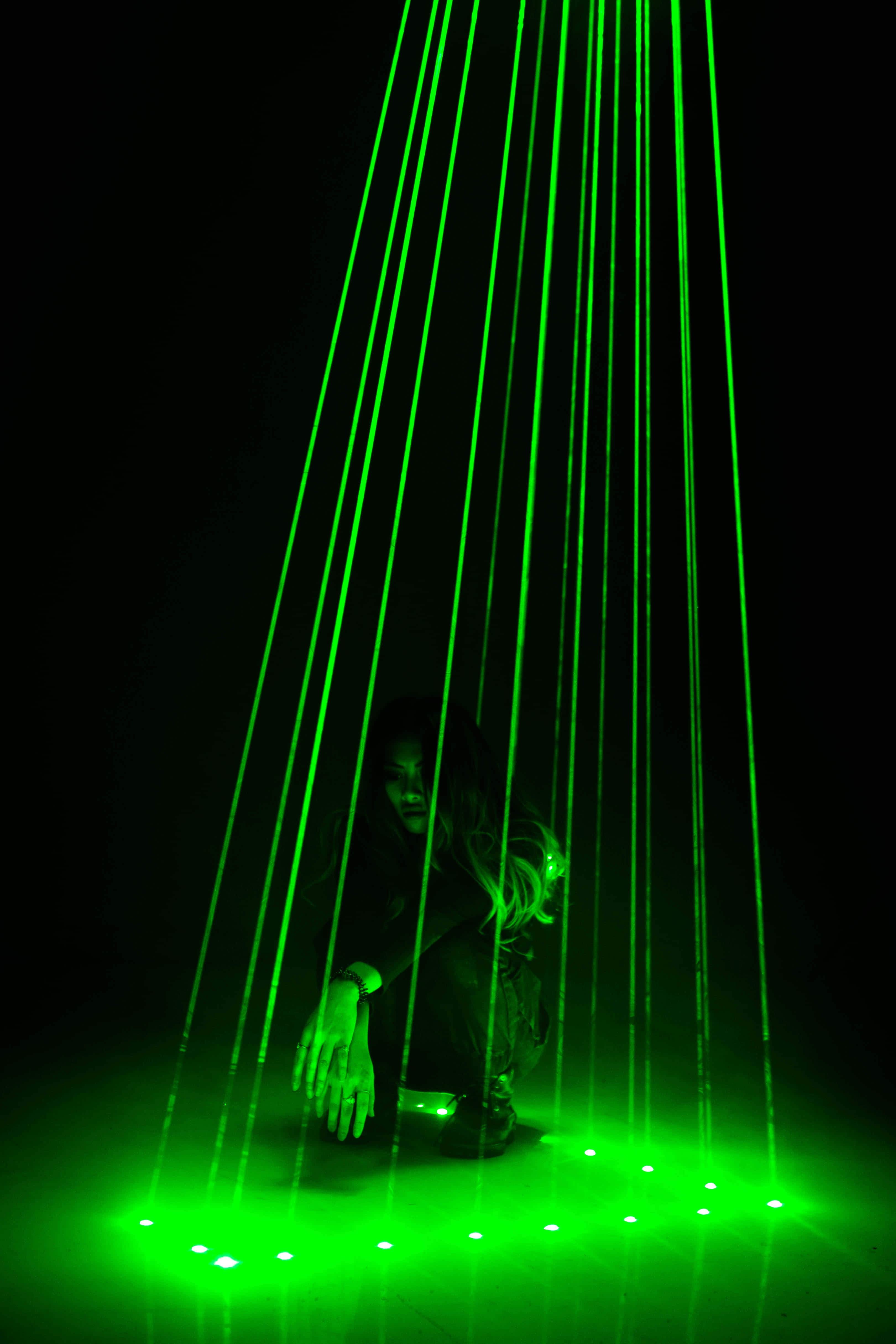 Laser 桌布 壁紙 — 一個人蹲在黑暗房間中傾瀉而下的綠色雷射光束下，地板上有發光的點。