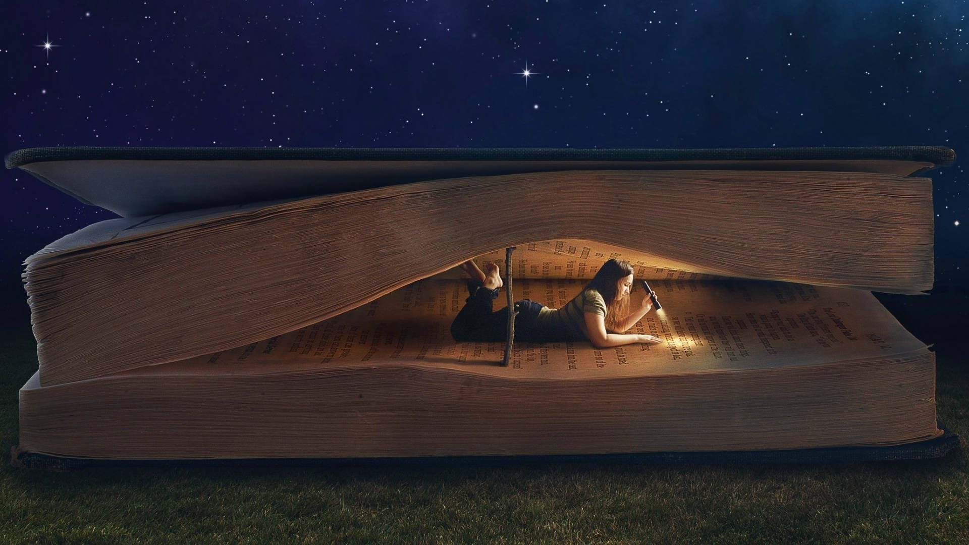 看書 桌布 壁紙 — 一個人躺在一個巨大的打開書本裡面閱讀，下方有草地，上方是滿天星斗的夜空。