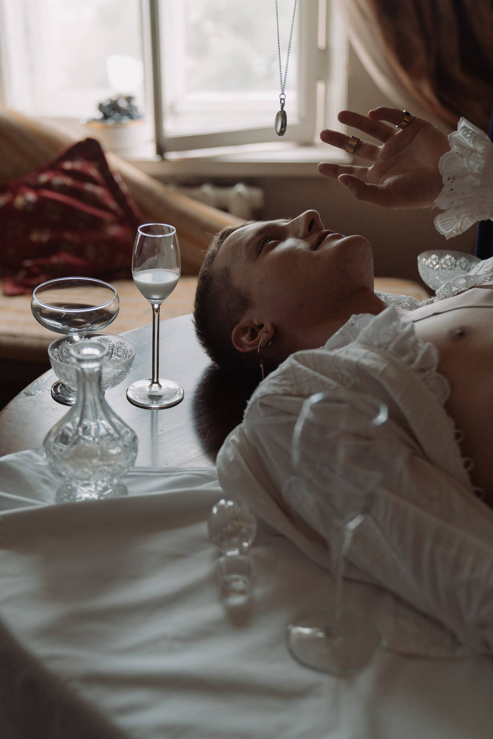 Hypnosis 桌布 壁紙 — 一個人躺在一張被玻璃器皿包圍的桌子上，另一隻手在窗邊向他們伸來。