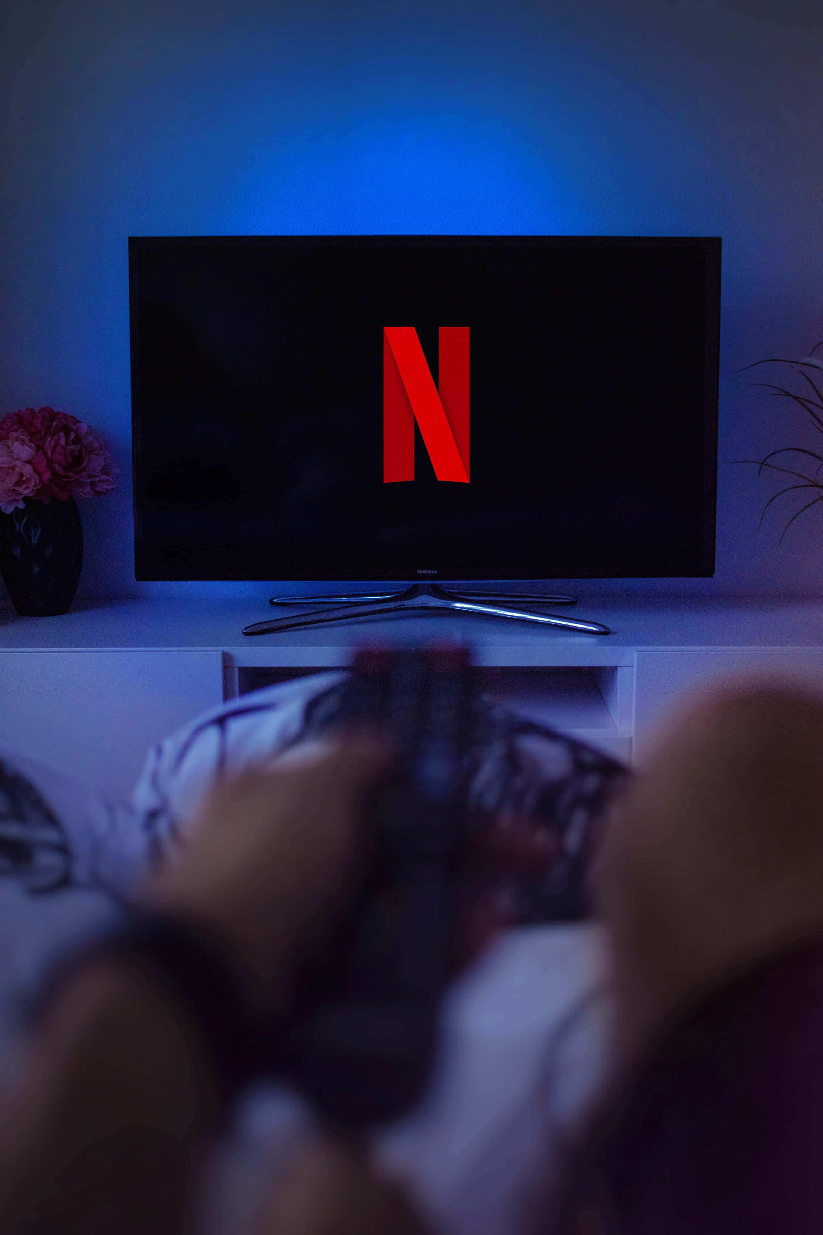 Netflix 桌布 壁紙 — 一個人躺在沙發上拿著遙控器，電視在藍色環境光下顯示紅色Netflix標誌。