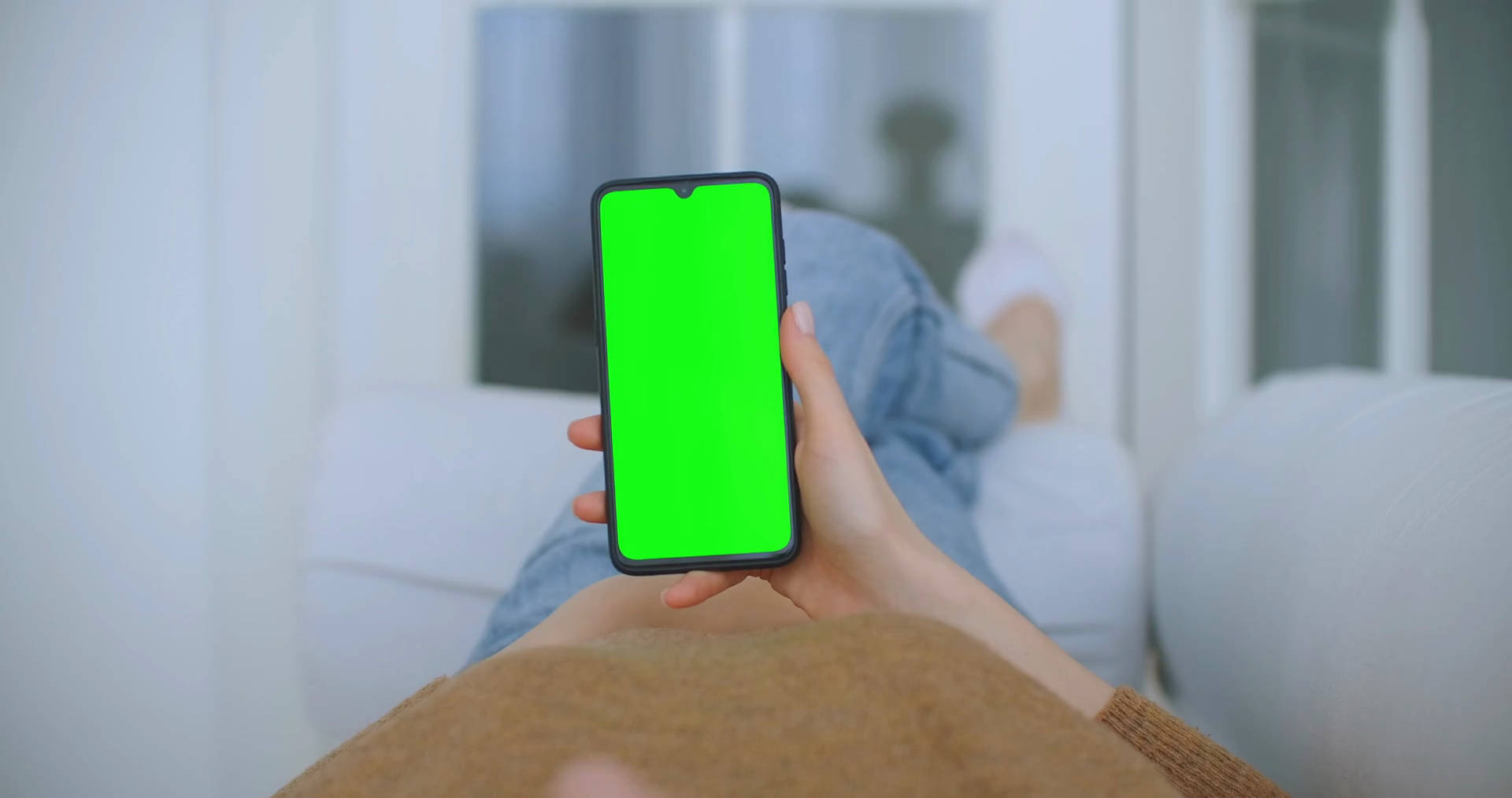 Green Screen 桌布 壁紙 — 一個人躺在白色沙發上，手持一部螢幕是亮綠色的智慧型手機。