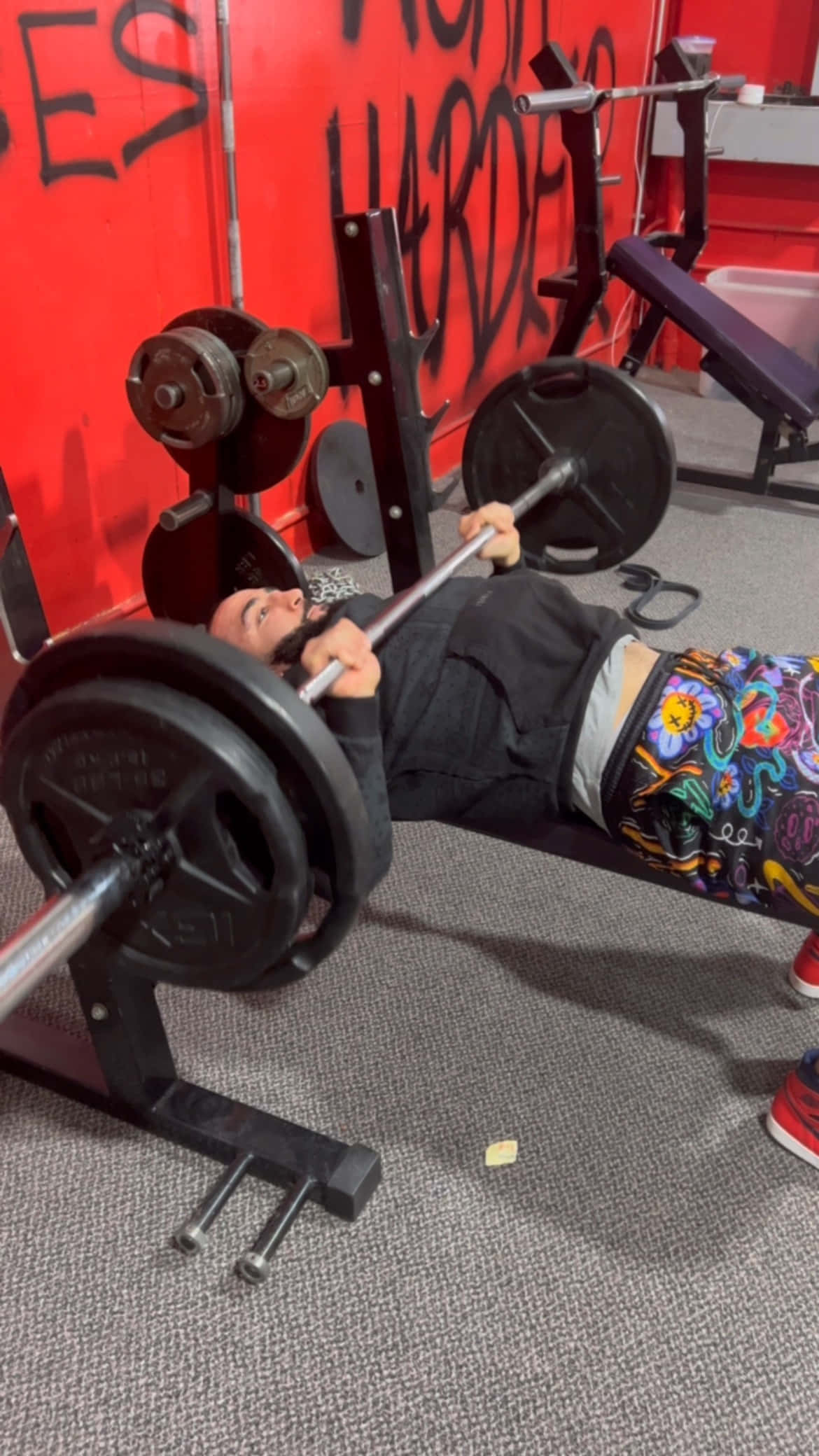 Fitness 桌布 壁紙 — 一個人躺在長椅上，在一個有紅色塗鴉牆和彩色圖案緊身褲的健身房裡推舉槓鈴。