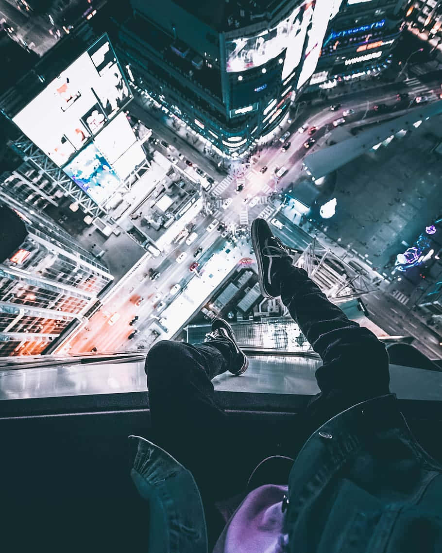 Rooftop 桌布 壁紙 — 一個人躺在高處的觀景點，俯瞰夜晚充滿霓虹燈光的城市景觀，下方有發光的廣告牌和繁忙的街道。