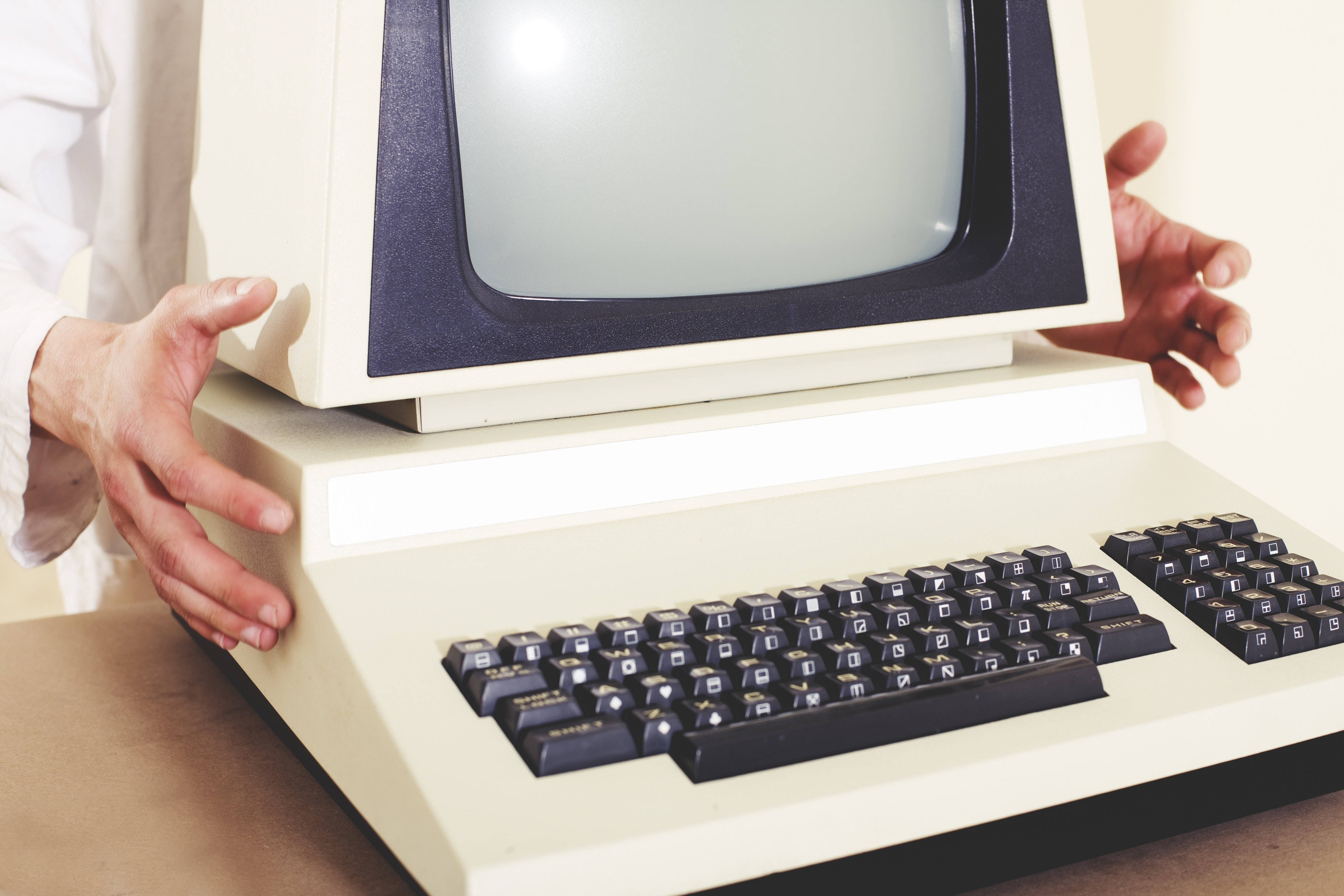 Computer Screen 桌布 壁紙 — 一個人輕輕地拿著一台復古米色電腦，內建顯示器和黑色鍵盤，放在木桌上。