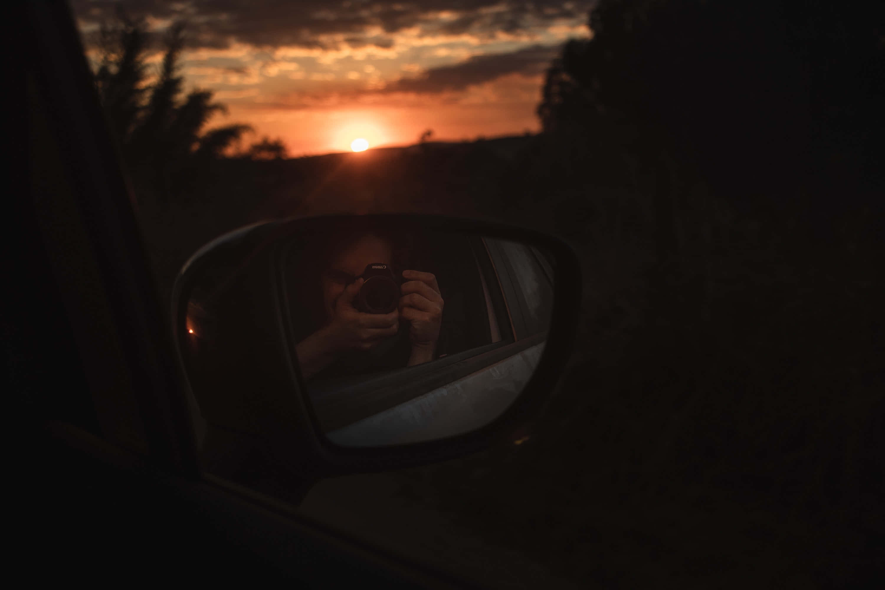 美學 桌布 壁紙 — 一個人透過汽車側鏡捕捉夕陽，鏡中映出他們的剪影，背景是火紅的橙色雲彩。