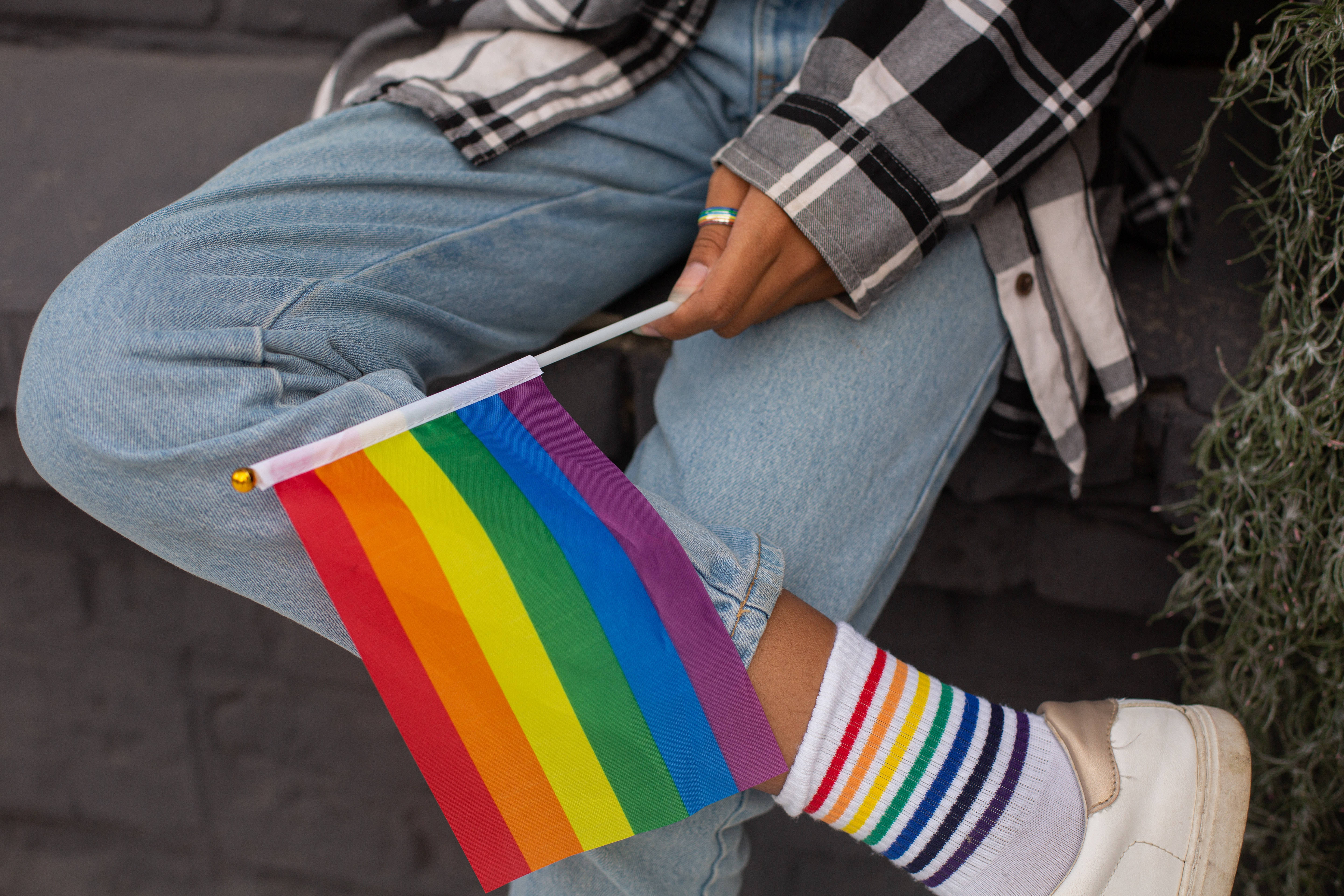 Pride Flag 桌布 壁紙 — 一個人隨意坐著，手持彩虹旗，穿著相配的彩虹襪子和牛仔褲。