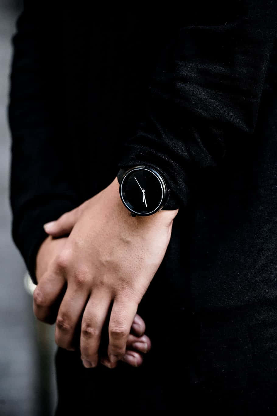 Mens Fashion 桌布 壁紙 — 一個人雙手合十，戴著一隻極簡黑色手錶，背景是深色有紋理的衣袖特寫。