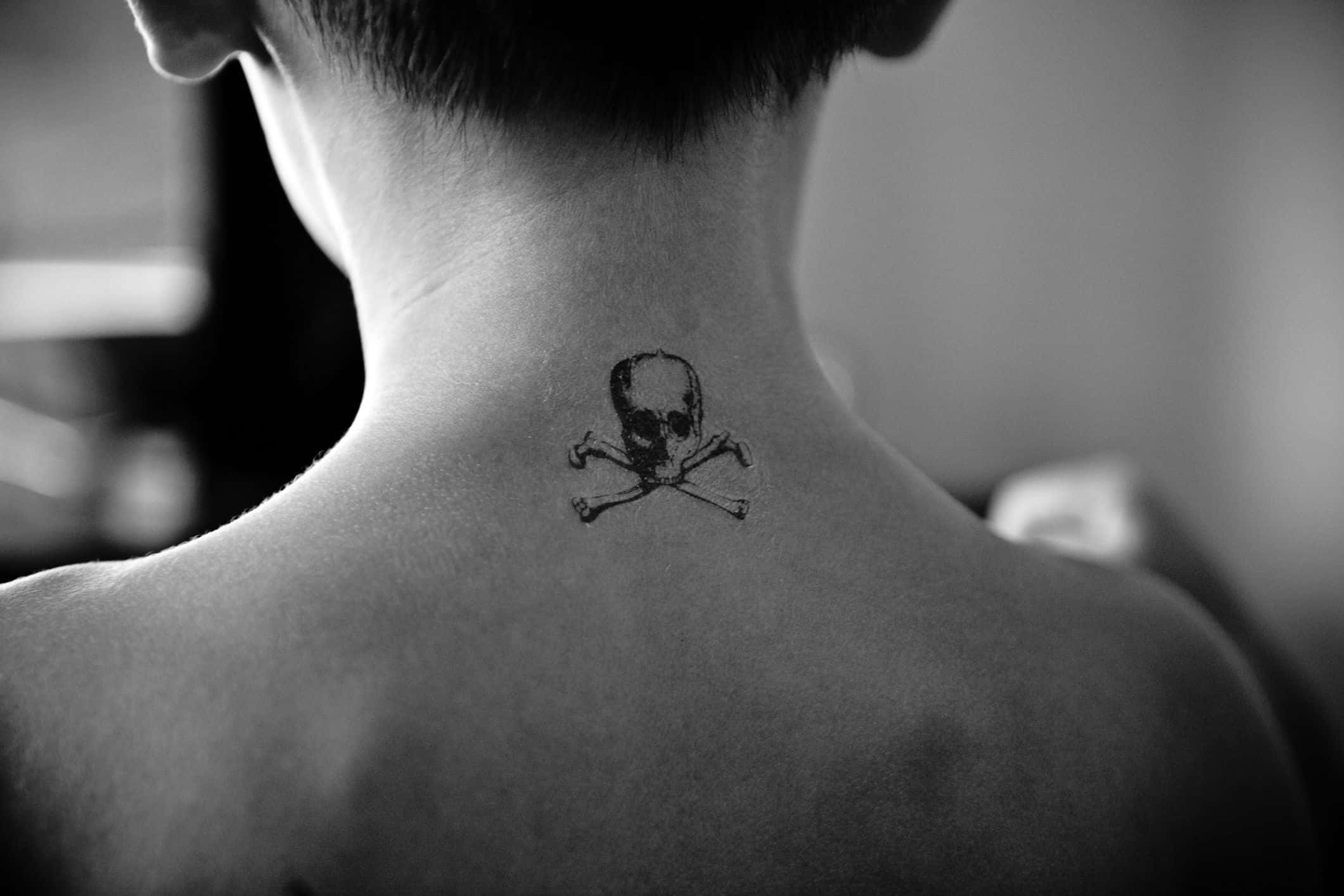 Halloween Tattoos 桌布 壁紙 — 一個人頸部的黑白特寫，上面有一個小小的骷髏頭和交叉骨紋身。