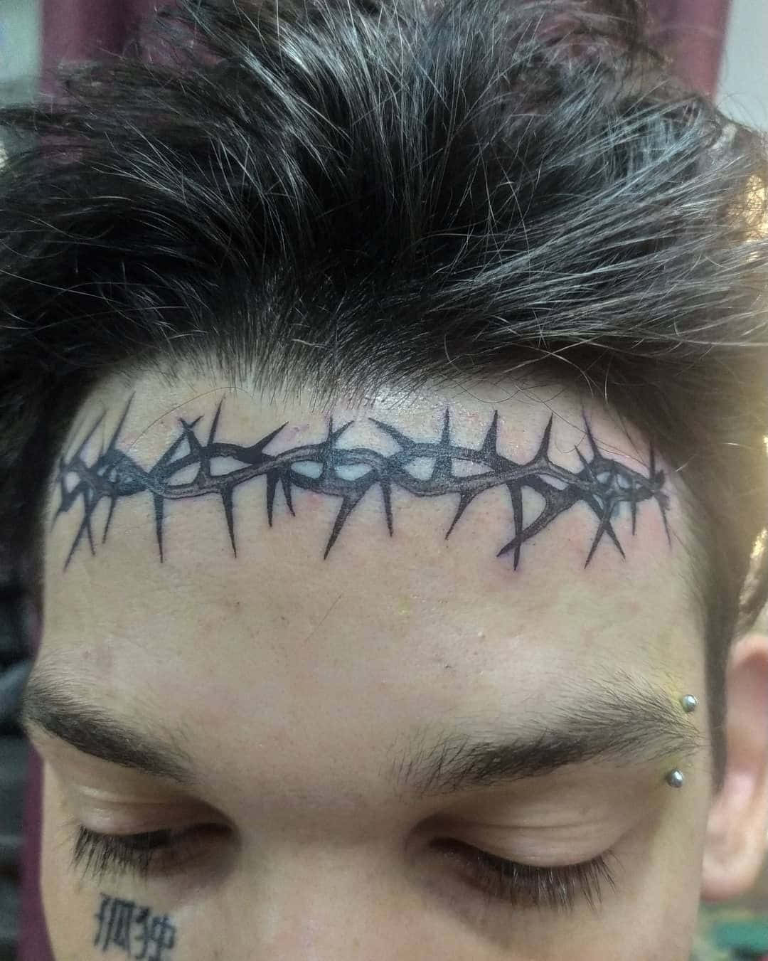 Face Tattoo 桌布 壁紙 — 一個人額頭的近照，上面有粗黑荊棘冠紋身和銀色耳環。