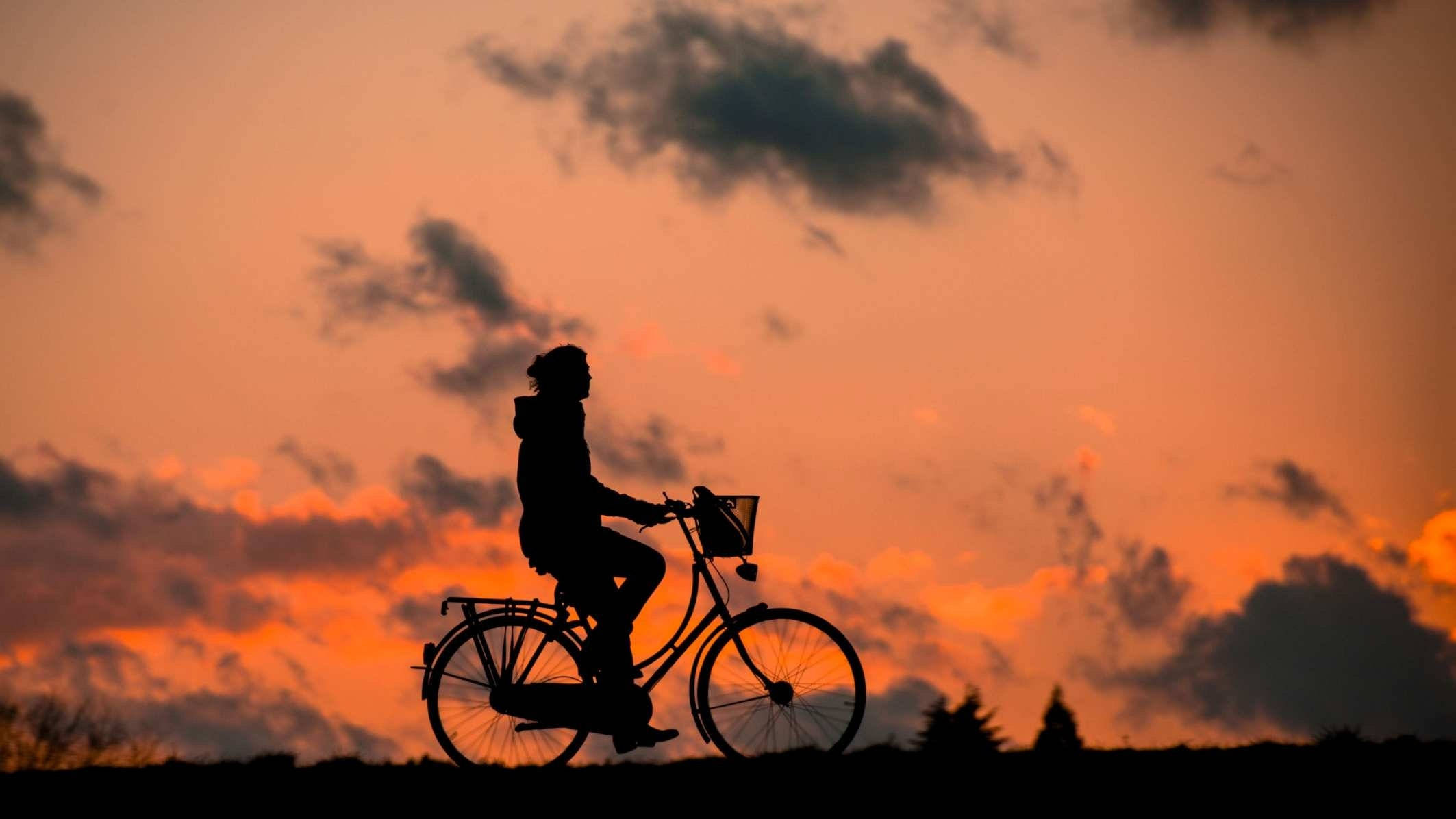 Silhouette 桌布 壁紙 — 一個人騎著腳踏車的剪影，背景是火紅的橙色日落天空，散落著雲朵。