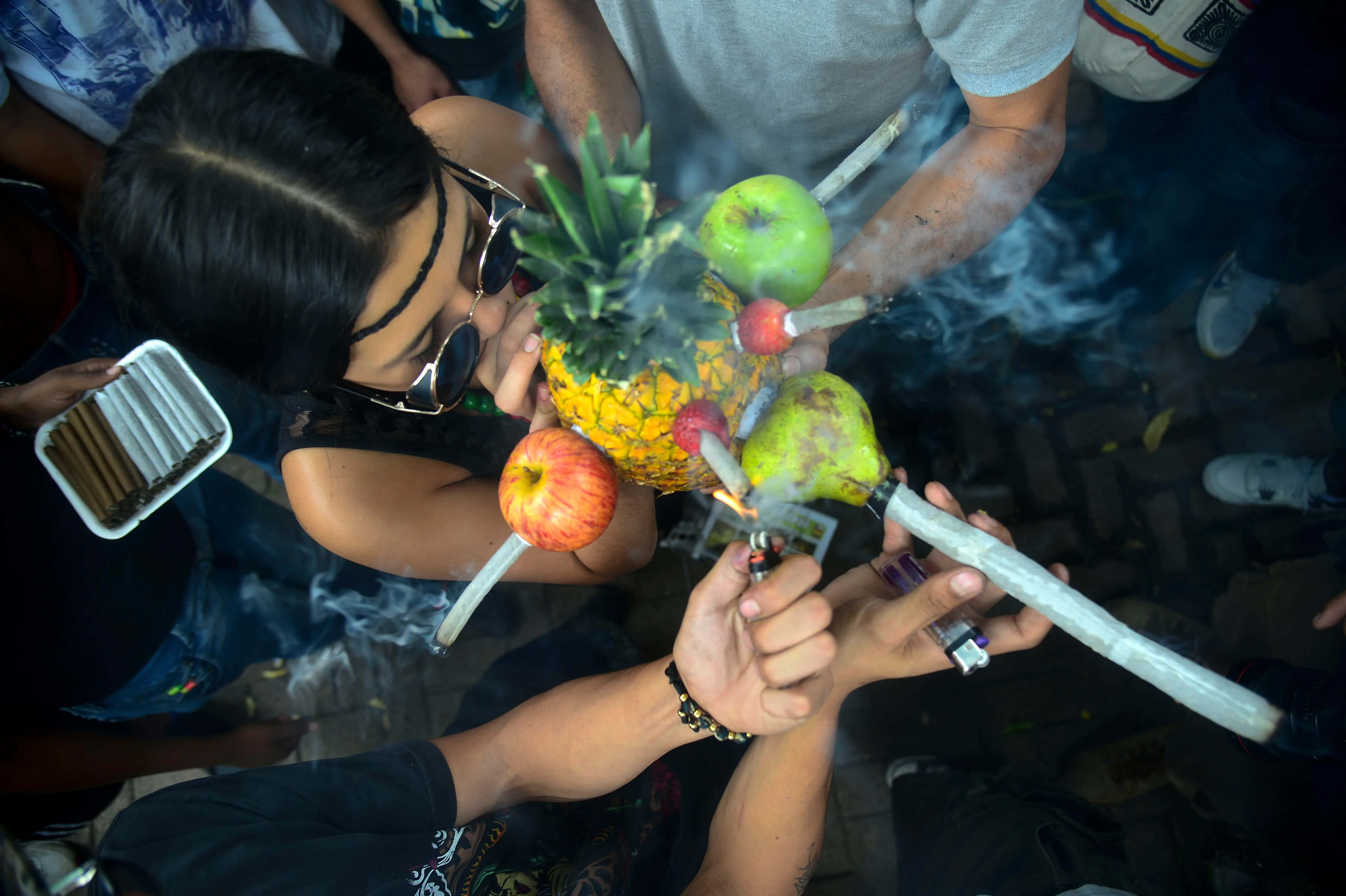 Weed Blunt 桌布 壁紙 — 一個人點燃插在鳳梨中的大麻煙，周圍有蘋果和梨，煙霧在他們周圍旋轉。