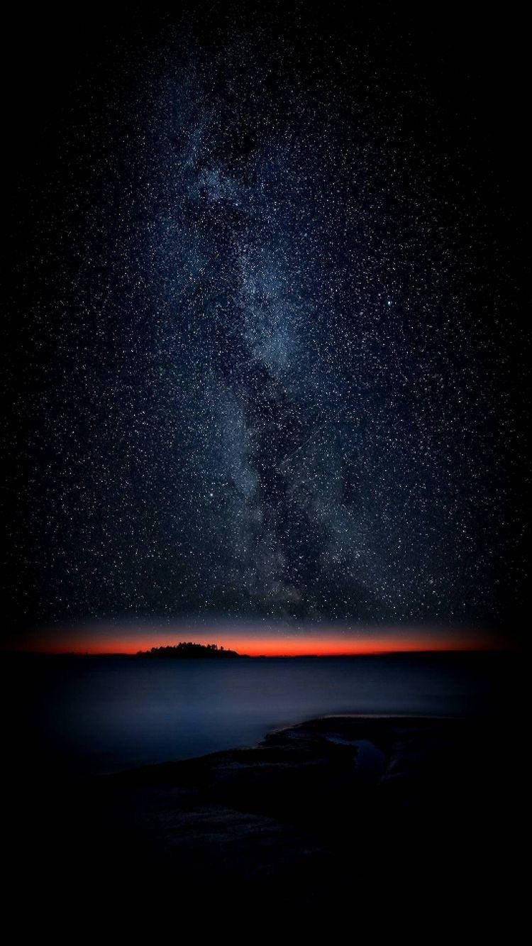 Stars 桌布 壁紙 — 一個令人嘆為觀止的夜空，佈滿星星，銀河在黑暗的岩石海岸線剪影上方拱起，地平線發出橙色的光芒。