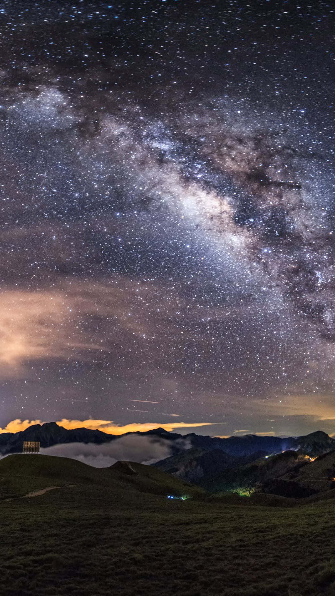 Galaxy Sky 桌布 壁紙 — 一個令人嘆為觀止的夜空，佈滿星星，銀河在下方有發光雲層的山脈景觀上拱起。