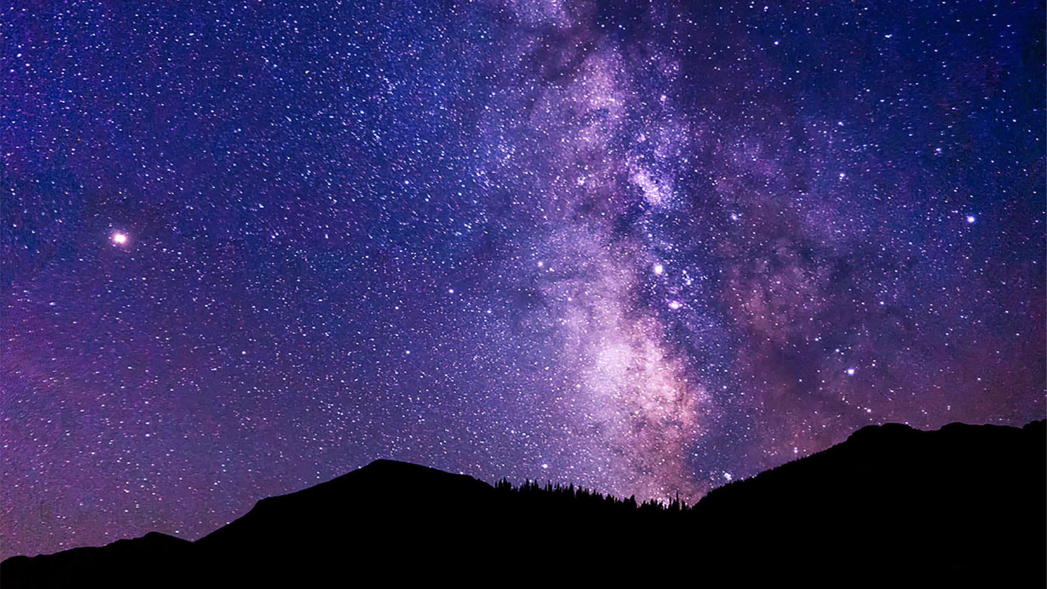銀河 桌布 壁紙 — 一個令人嘆為觀止的夜空，佈滿星星和銀河，拱形在黑暗的山脈輪廓之上。