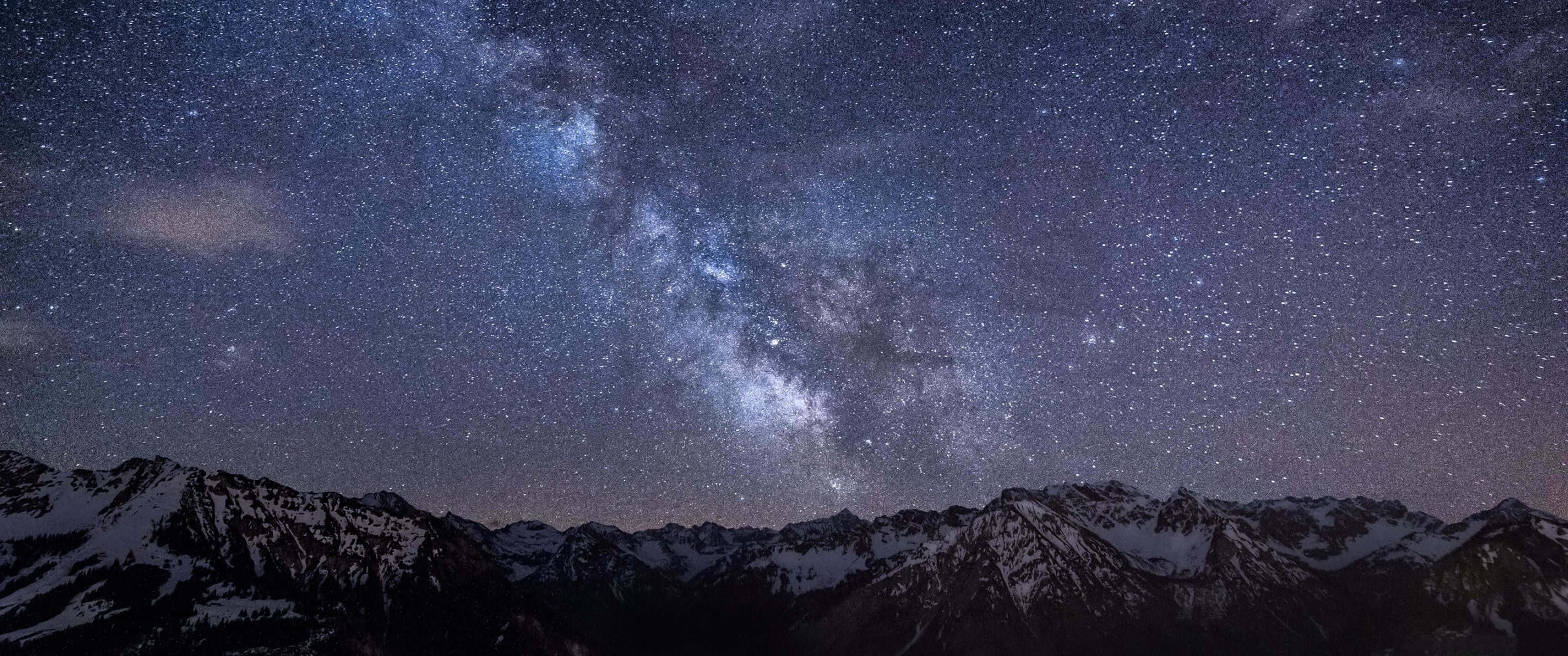 Aesthetic Nature 桌布 壁紙 — 一個令人嘆為觀止的夜空，充滿無數星星，銀河系雄偉地拱起在積雪的山脈之上。