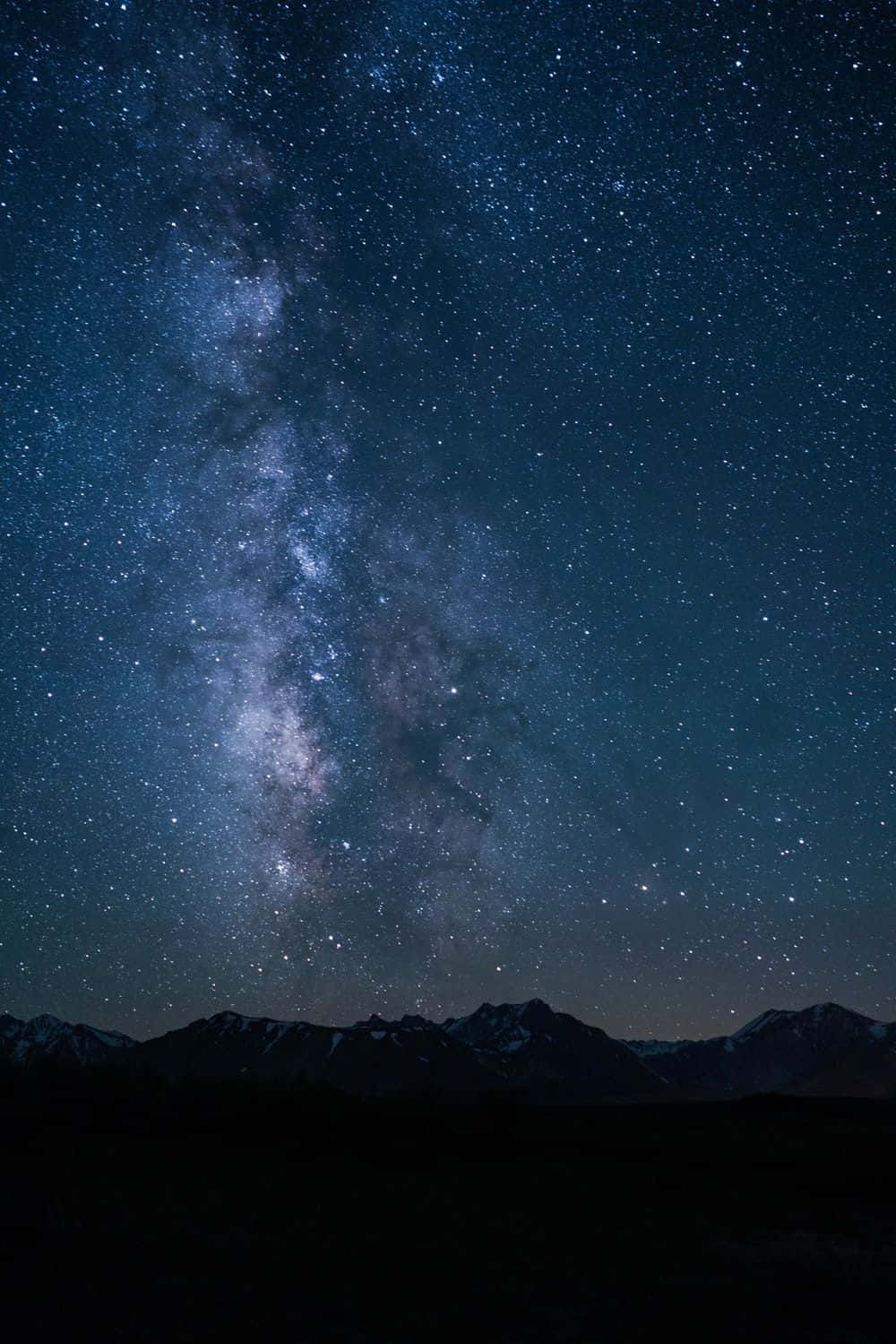 Dark Sky 桌布 壁紙 — 一個令人嘆為觀止的夜空，充滿無數星星，發光的銀河在黑暗的山脈輪廓上拱起。