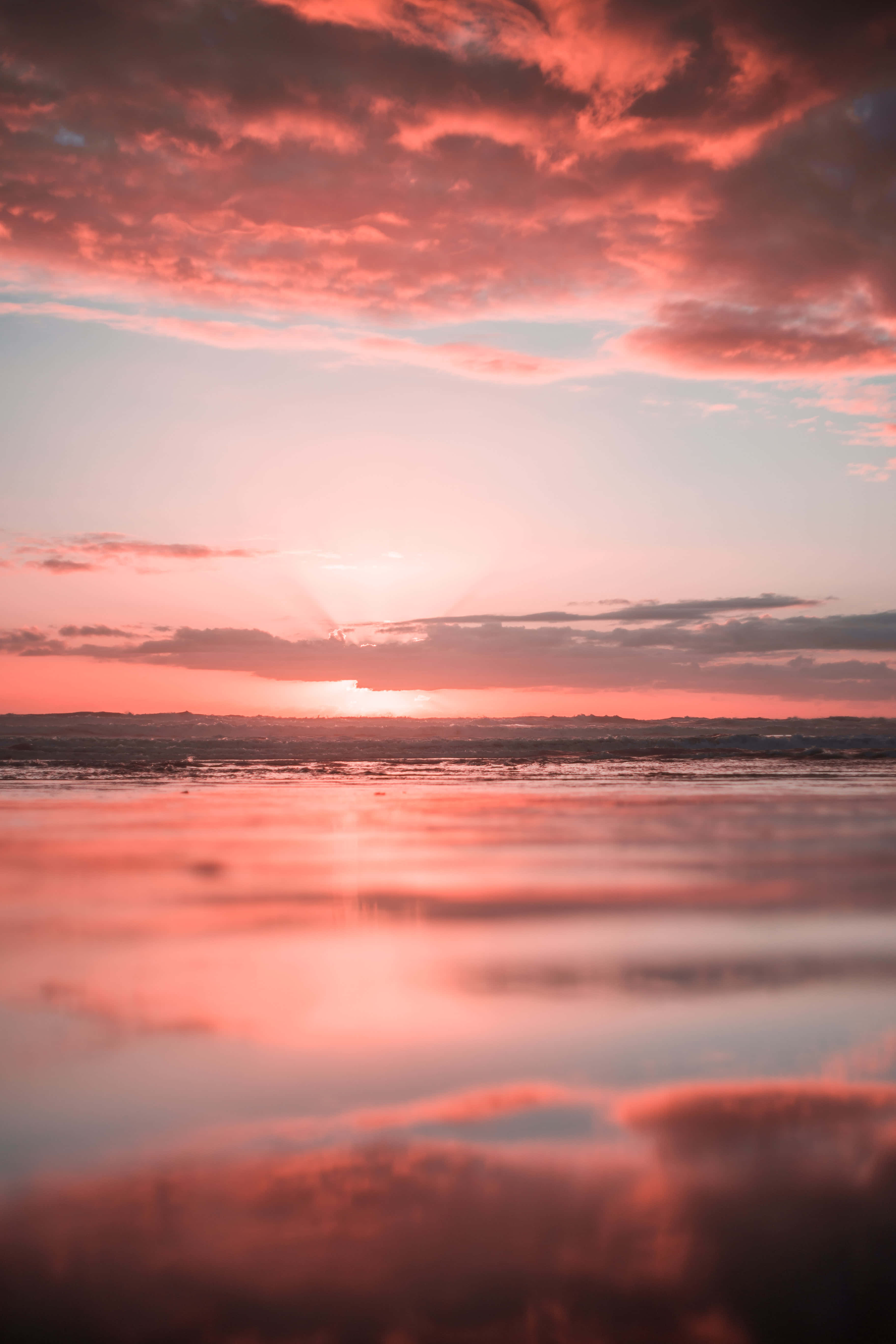 Pink Beach Sunset 桌布 壁紙 — 一個令人嘆為觀止的日落，映照在濕漉漉的沙灘上，火紅的粉紅雲彩倒映在淺水中。