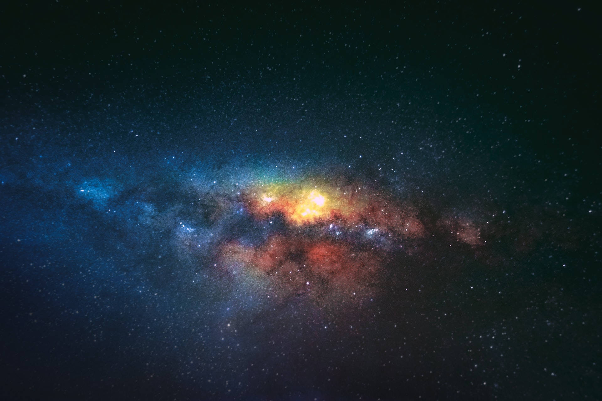 夜空 桌布 壁紙 — 一個令人嘆為觀止的景色，展現出一個充滿活力的星系，在佈滿星辰的宇宙背景下，散發著橙色和藍色的星雲光芒。