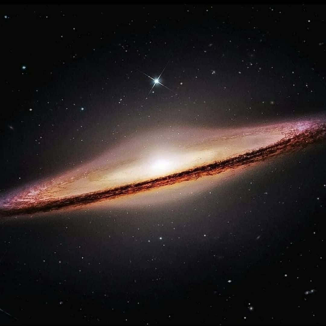 Sombrero Galaxy 桌布 壁紙 — 一個令人嘆為觀止的螺旋星系，在佈滿星辰的宇宙虛空中散發著溫暖的橙色和粉紅色調。