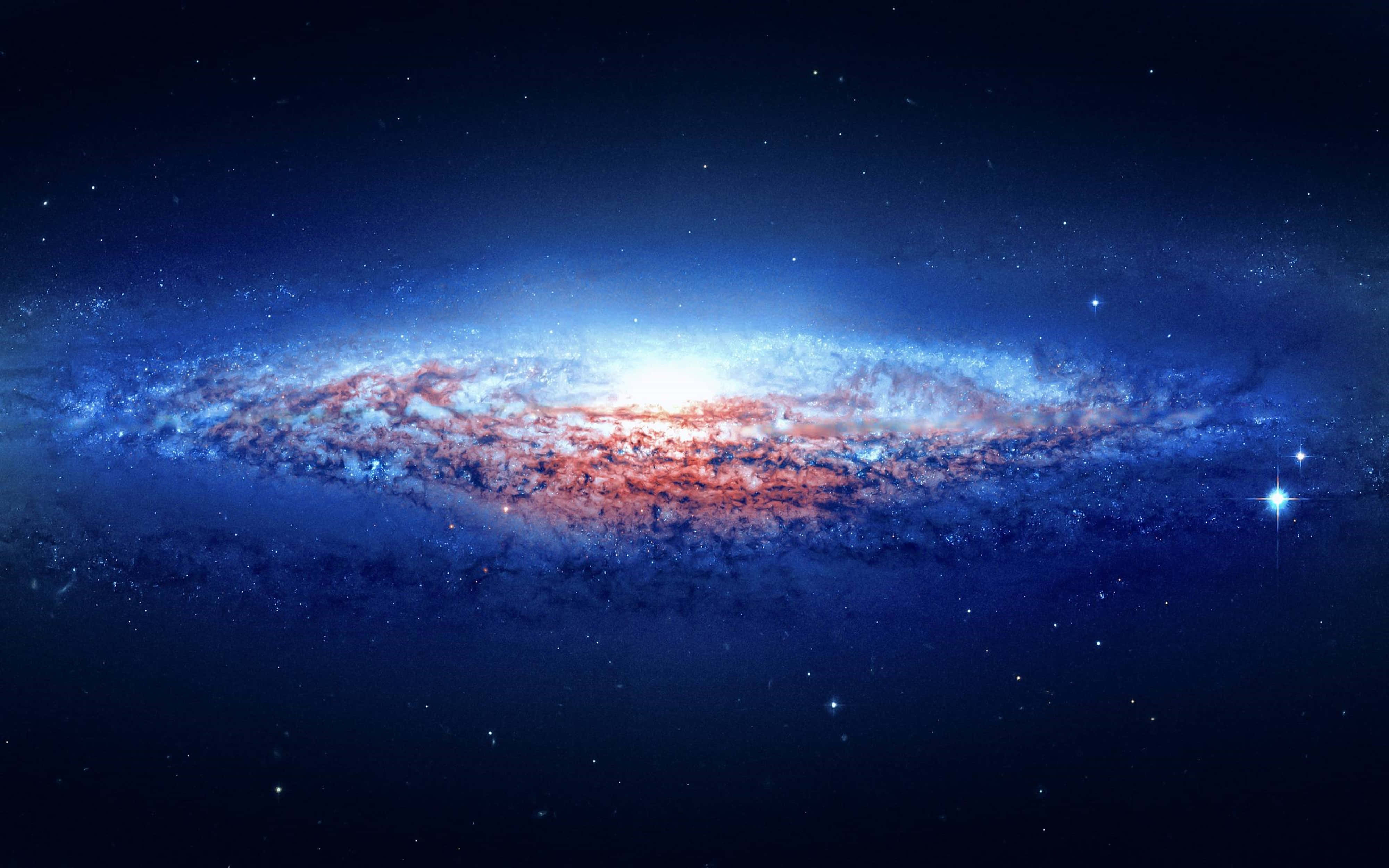 銀河 桌布 壁紙 — 一個令人嘆為觀止的螺旋星系，在繁星點點的宇宙背景下閃耀著藍色和火紅色的色調。