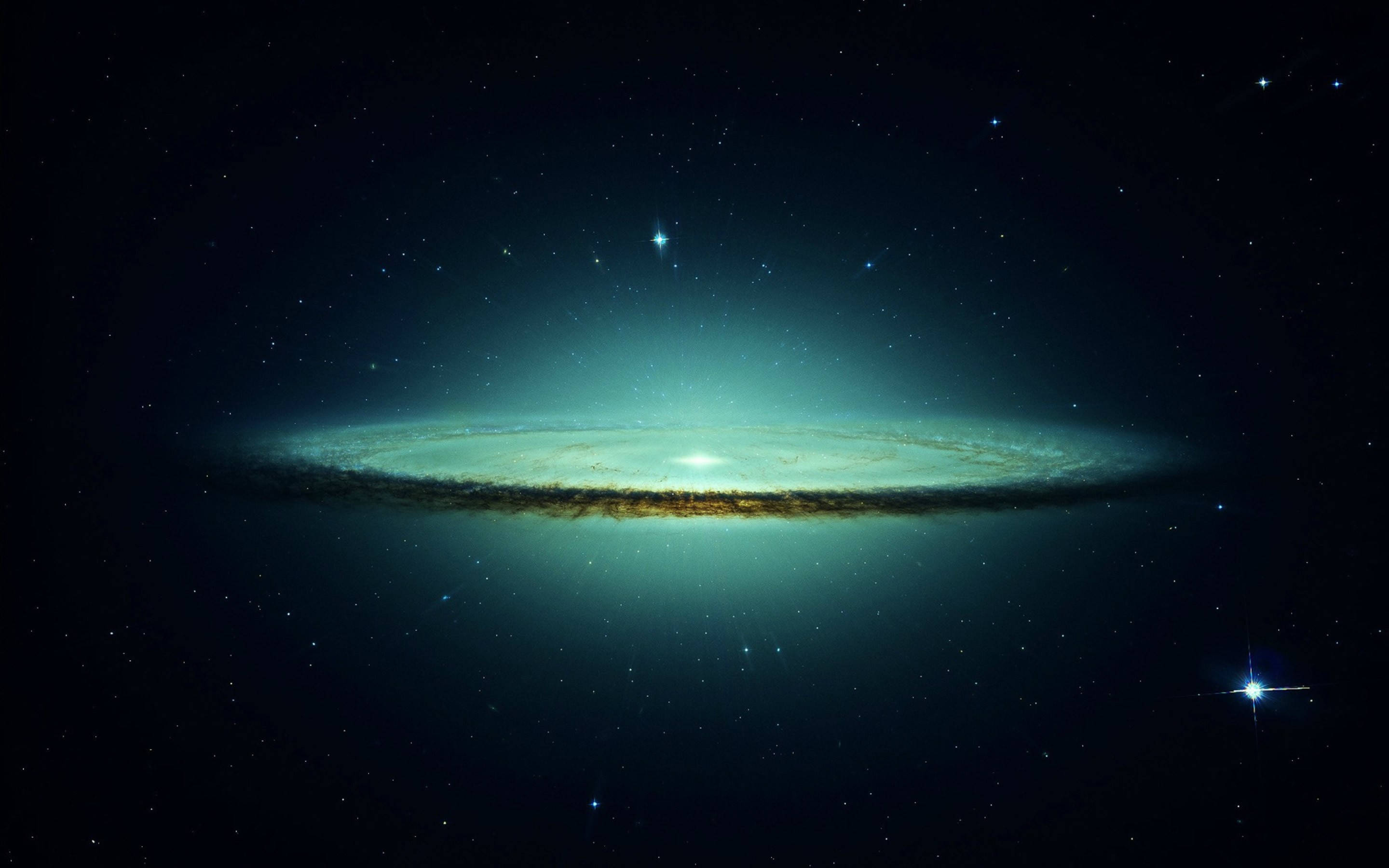 外太空 桌布 壁紙 — 一個令人嘆為觀止的螺旋星系，在繁星點點的宇宙背景下散發著青綠色和金色的光芒。