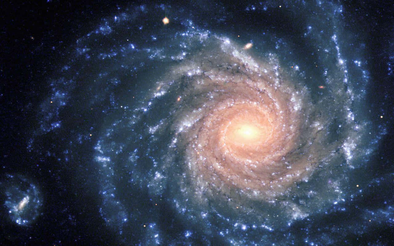 Spiral Galaxy 桌布 壁紙 — 一個令人嘆為觀止的螺旋星系，帶有發光的橙色核心和充滿恆星及宇宙塵埃的旋轉藍色旋臂。