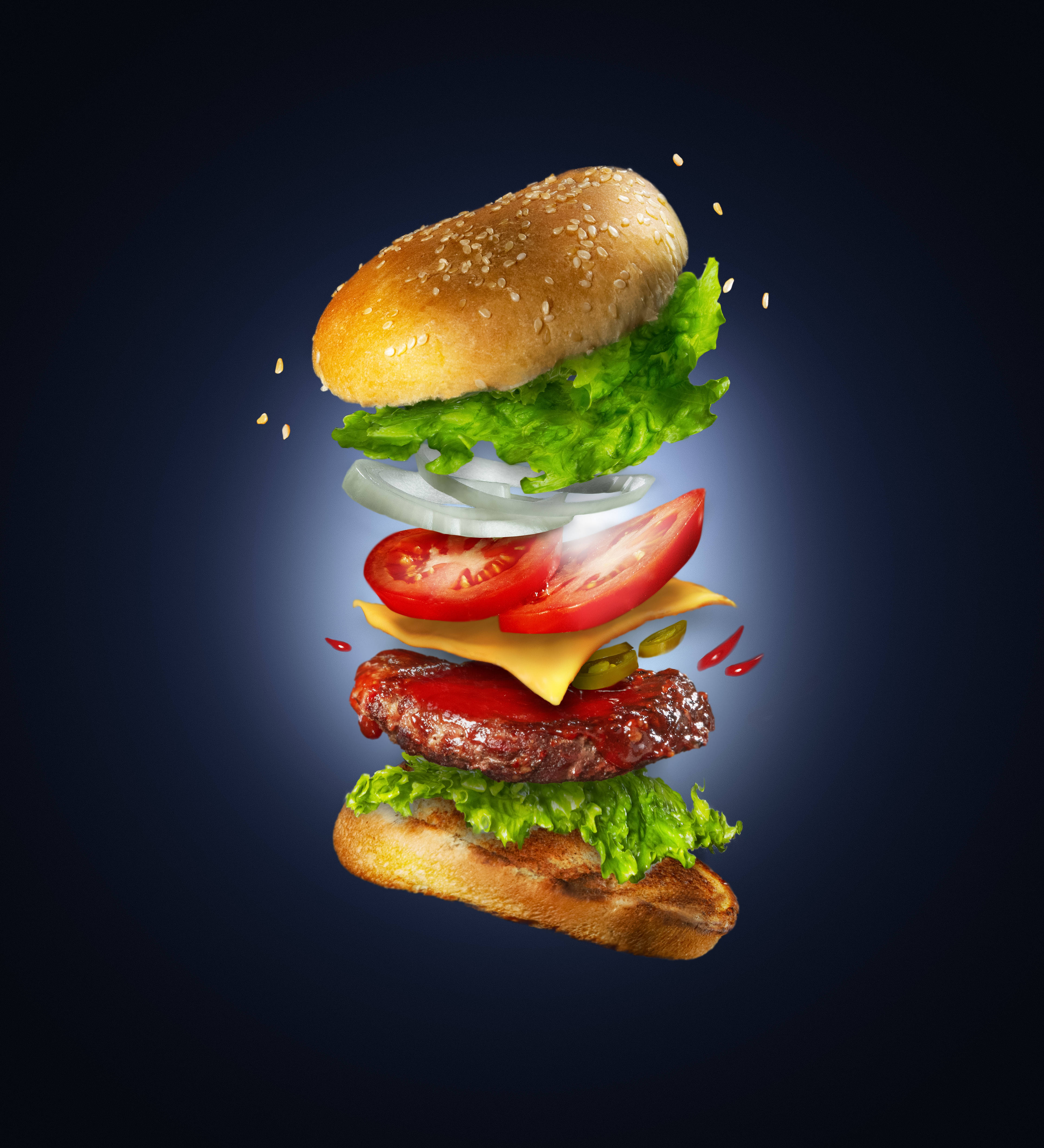 Food Photography 桌布 壁紙 — 一個令人垂涎的漢堡懸浮在半空中，各層分離，背景為深藍色漸變。