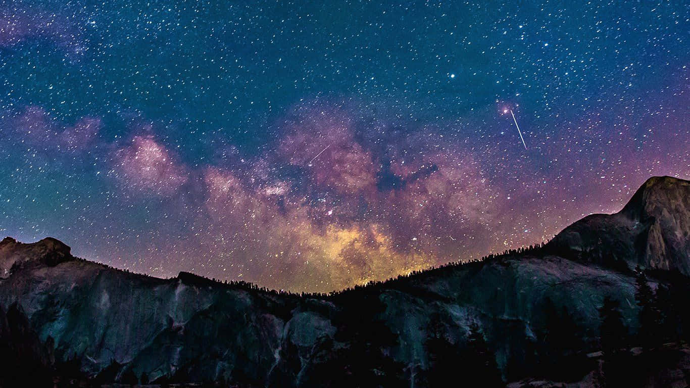 美學 桌布 壁紙 — 一個令人屏息的夜空，佈滿繁星和閃爍的銀河，拱形橫跨在黑暗的山峰剪影之上。