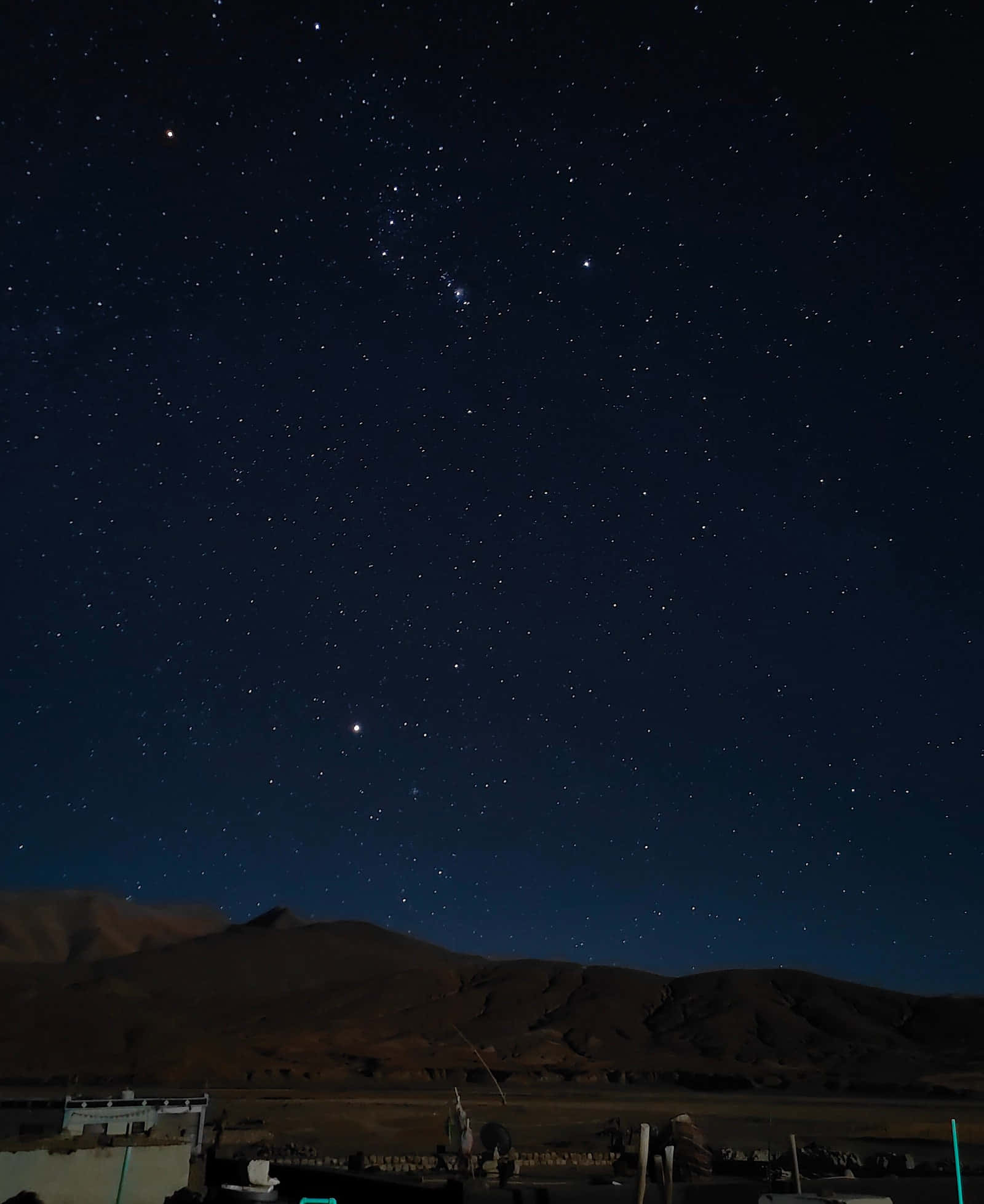 夜空 桌布 壁紙 — 一個令人屏息的夜空，充滿無數星星，拱形跨越黑暗的輪廓山脈和下方寧靜的村莊。