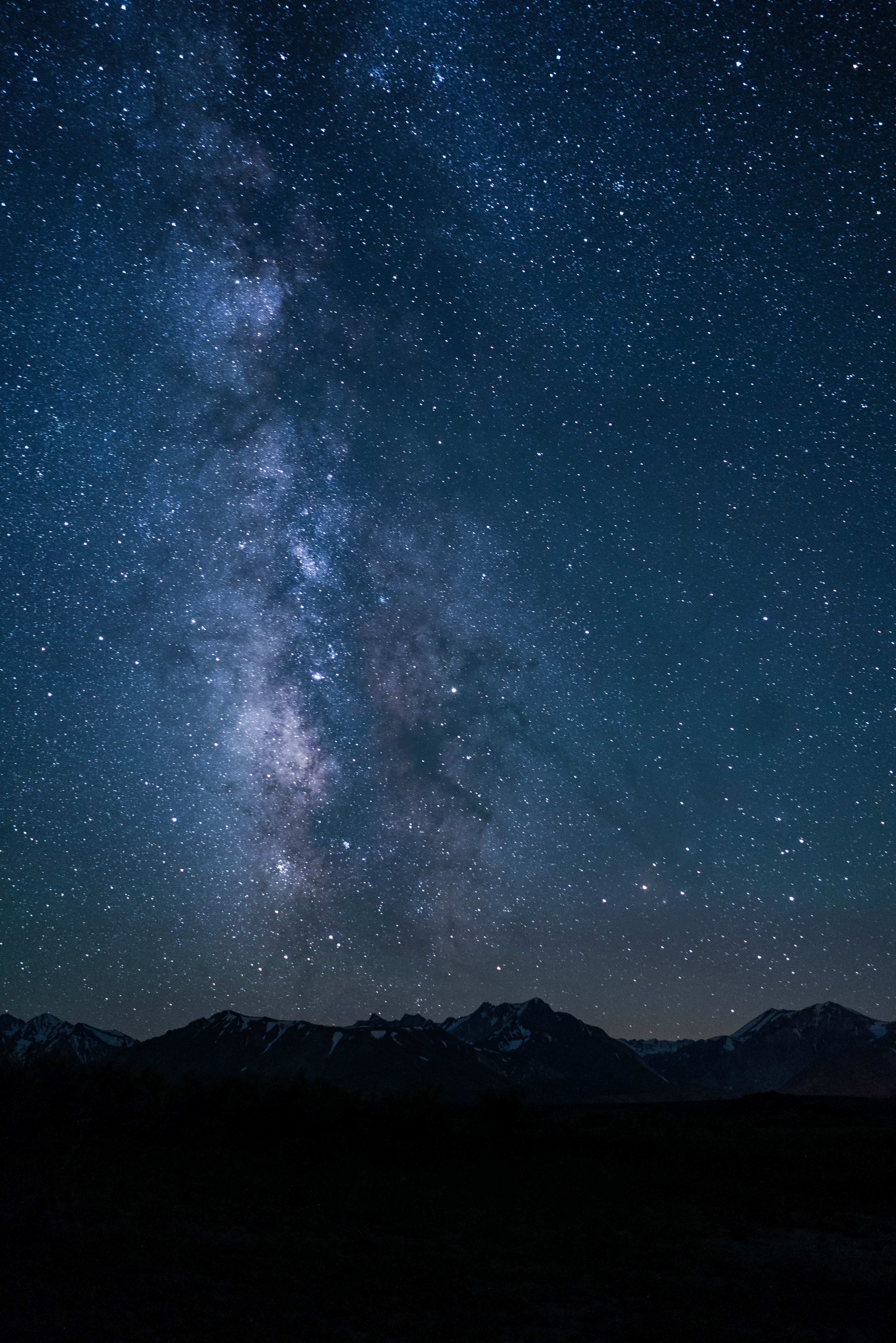 Starry Sky 桌布 壁紙 — 一個令人屏息的夜空，充滿無數星星和銀河，在黑暗的山脈輪廓上拱起。