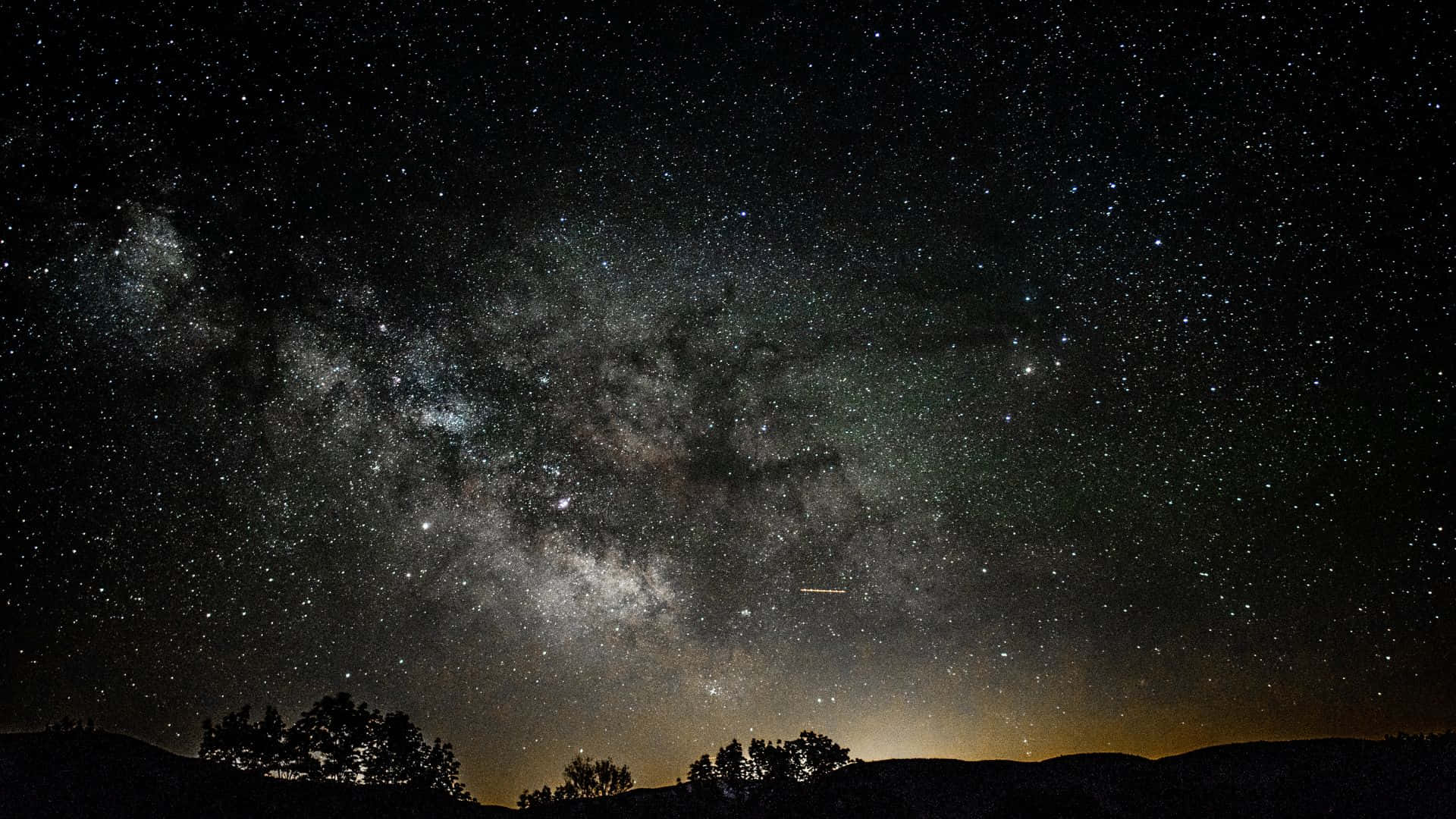 黑夜 桌布 壁紙 — 一個令人屏息的夜空，充滿無數星星和銀河，拱形跨越黑暗的山脈和樹木剪影。
