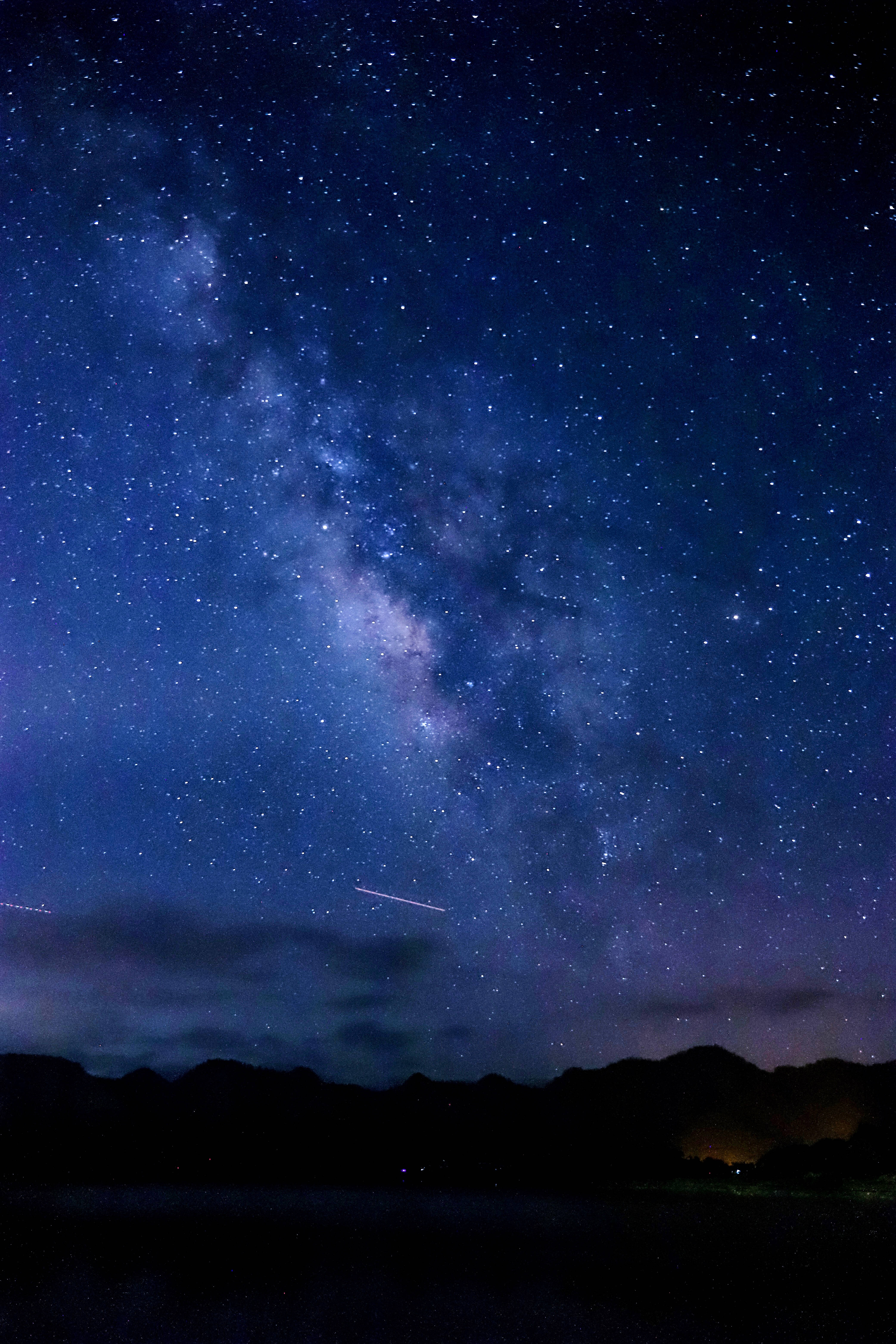 Blue Galaxy 桌布 壁紙 — 一個令人屏息的夜空，充滿無數星星，閃爍的銀河在黑暗的山脈剪影和寧靜的湖泊上方拱起。