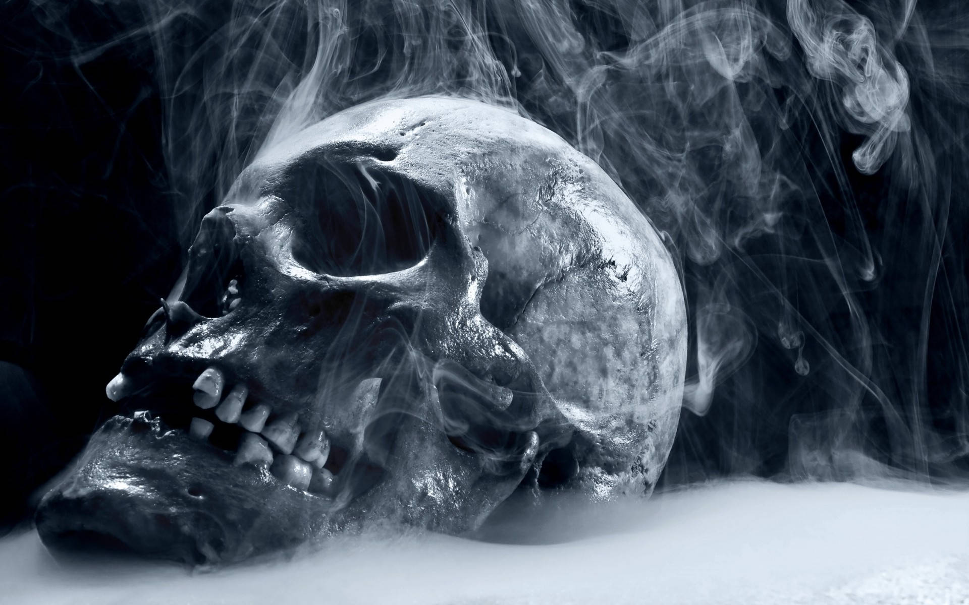 HD Skull 桌布 壁紙 — 一個令人毛骨悚然的人類頭骨從黑暗背景中旋轉的煙霧中浮現，空洞的眼睛以詭異的靜止凝視著。