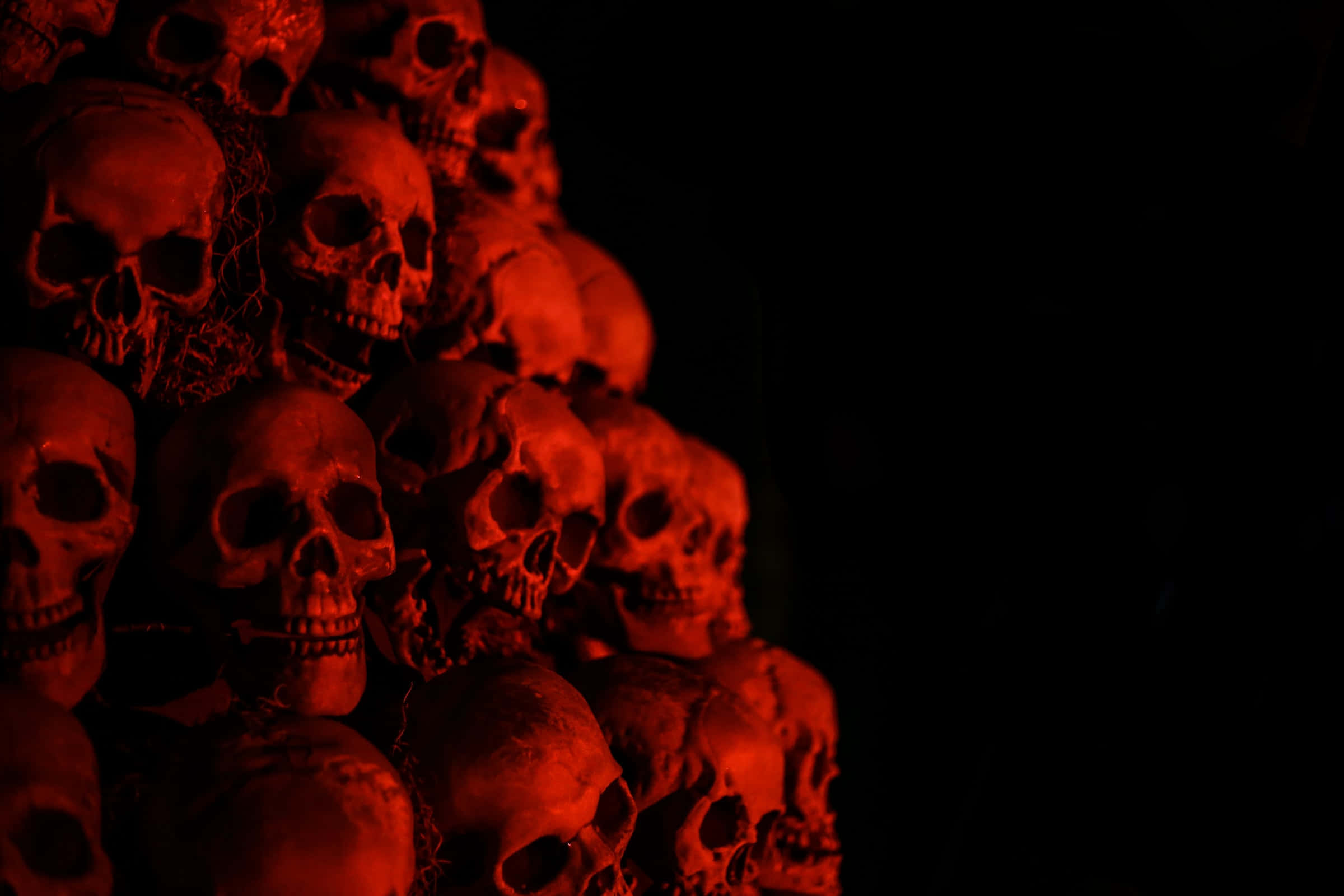 Halloween Skeleton 桌布 壁紙 — 一個令人毛骨悚然的人類頭骨金字塔，沐浴在詭異的紅光中，背景是漆黑的虛空。