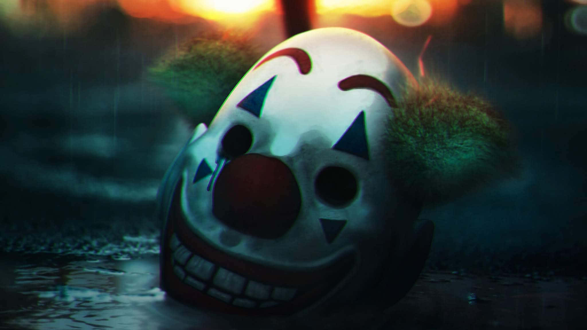 Smile 桌布 壁紙 — 一個令人毛骨悚然的小丑面具在泥濘的水中漂浮，天空是火燒般的日落，下著雨。