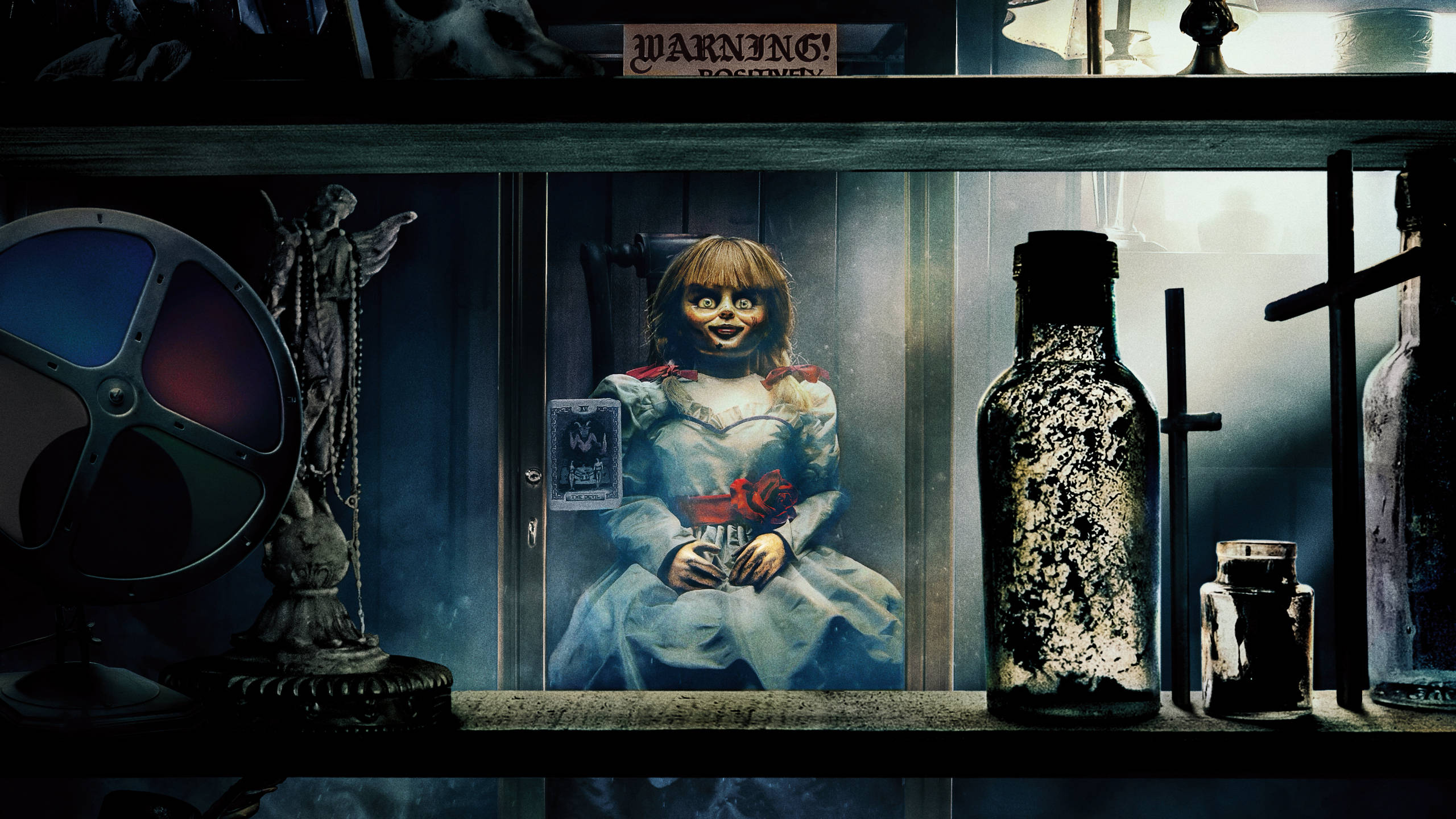 Annabelle 桌布 壁紙 — 一個令人毛骨悚然的展示櫃中，有一個大眼睛、手持紅玫瑰的恐怖娃娃，周圍環繞著陰森的古物，燈光昏暗。