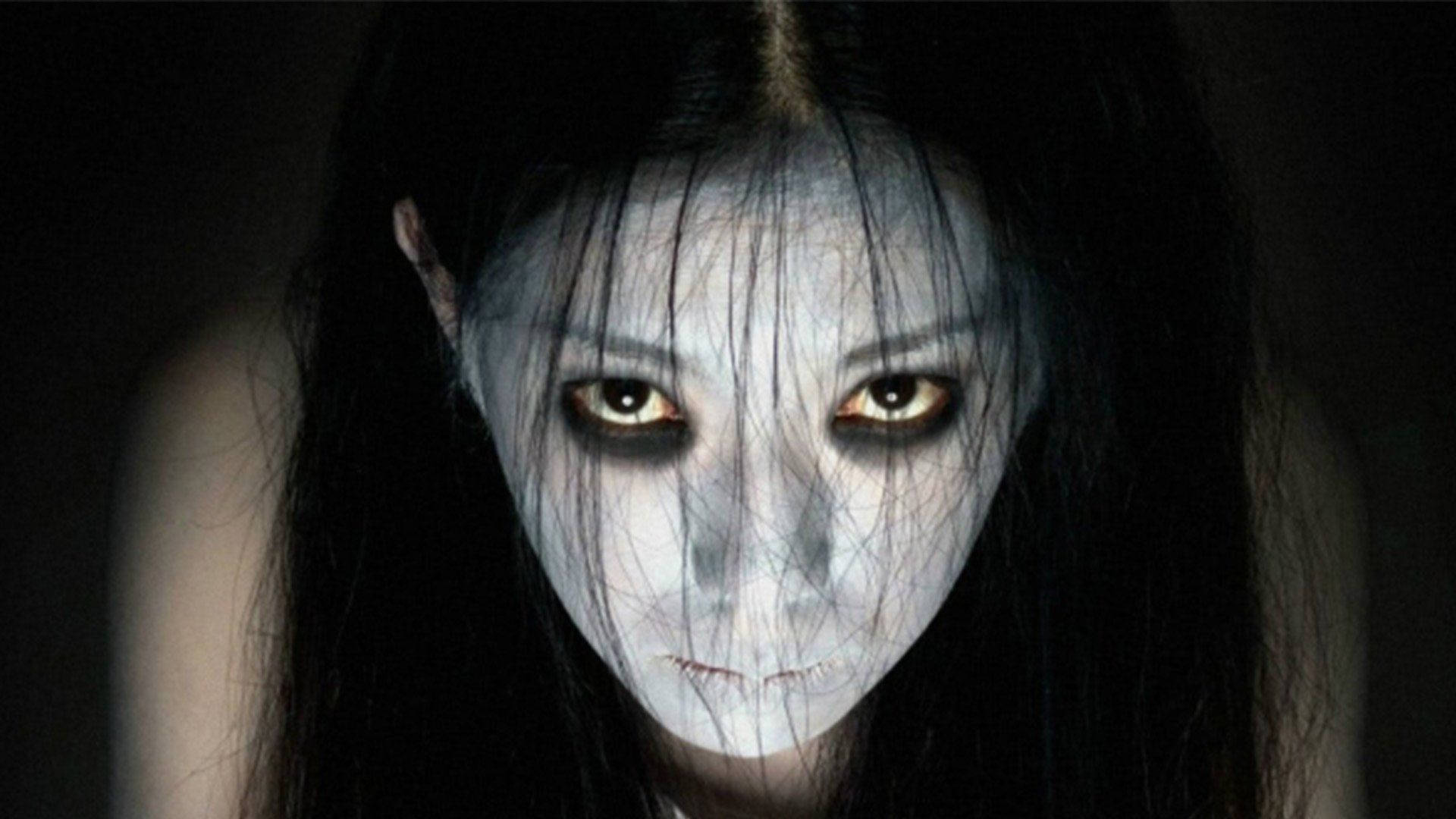 horror villains 桌布 壁紙 — 一個令人毛骨悚然的特寫，一個蒼白鬼魅的女人，有著發光的琥珀色眼睛和黑色頭髮，背景是黑色。