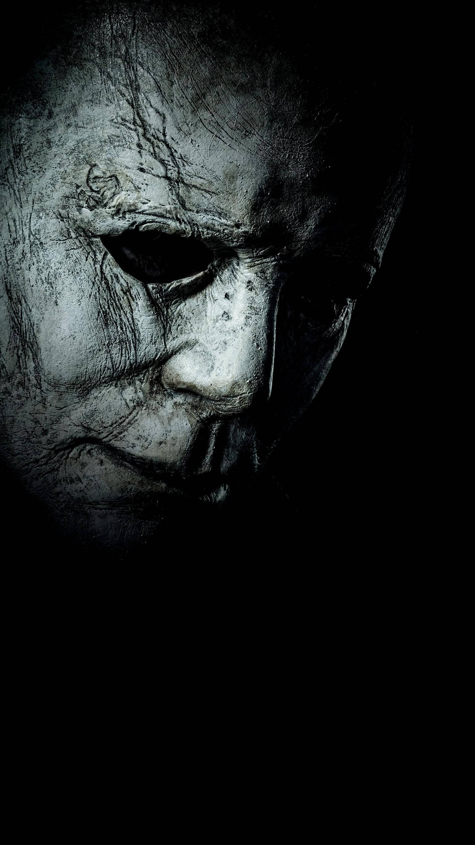 horror villains 桌布 壁紙 — 一個令人毛骨悚然的特寫，一個風化的白色面具，帶有深深的裂縫和黑色的眼窩，背景為黑色。