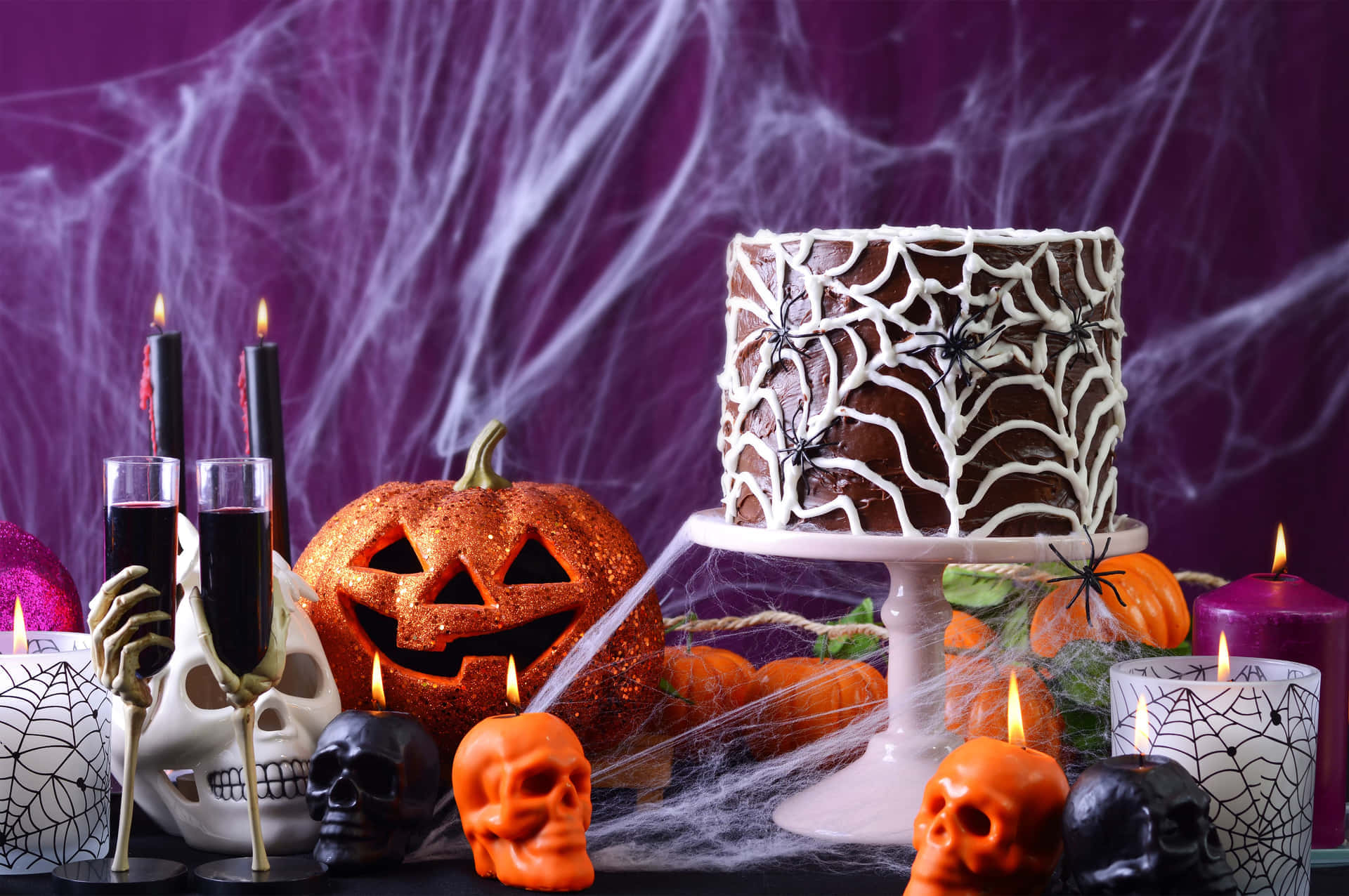 Halloween Props 桌布 壁紙 — 一個令人毛骨悚然的萬聖節甜點桌，上面有蜘蛛網蛋糕、發光南瓜和骷髏蠟燭，背景是紫色蜘蛛網。