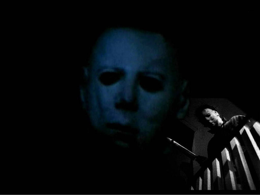 michael 桌布 壁紙 — 一個令人毛骨悚然的藍色恐怖場景，Michael Myers 戴著面具在黑暗中潛伏，籬笆後面還有另一個人影。