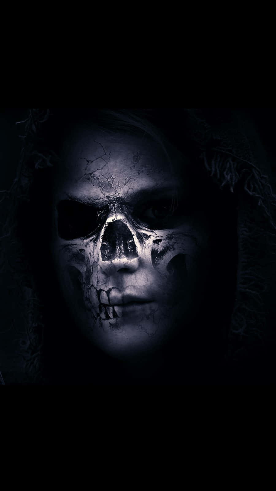 Aesthetic iPhone Horror 桌布 壁紙 — 一個令人毛骨悚然的近距離特寫，一個人的臉部分被裂開的頭骨面具遮蓋，在昏暗的藍色燈光下。