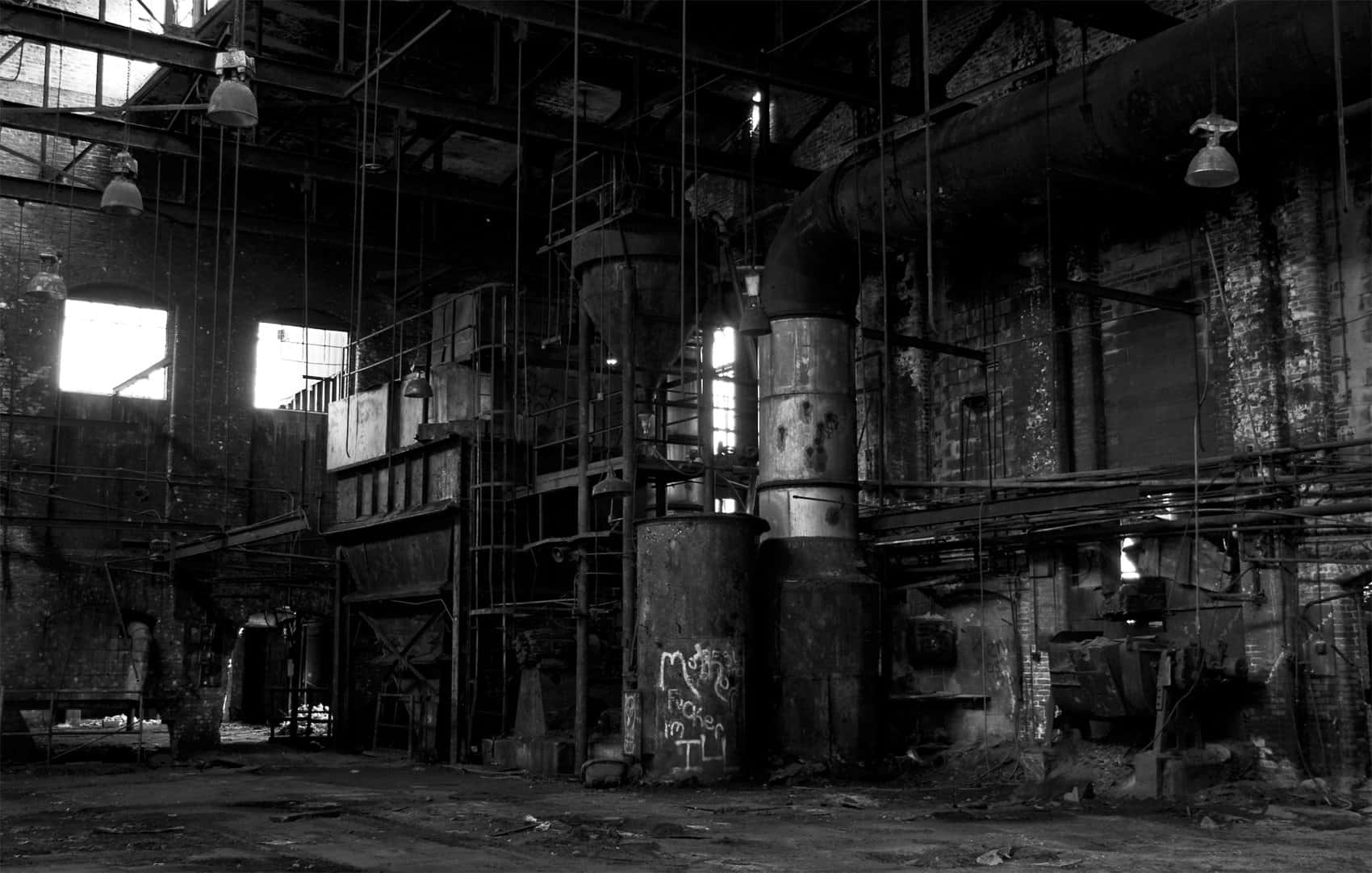 Industrial 桌布 壁紙 — 一個令人毛骨悚然的黑白景觀，展示了一個廢棄的工業工廠，有生鏽的管道、塗鴉和破損的窗戶，讓強烈的光線照射進來。