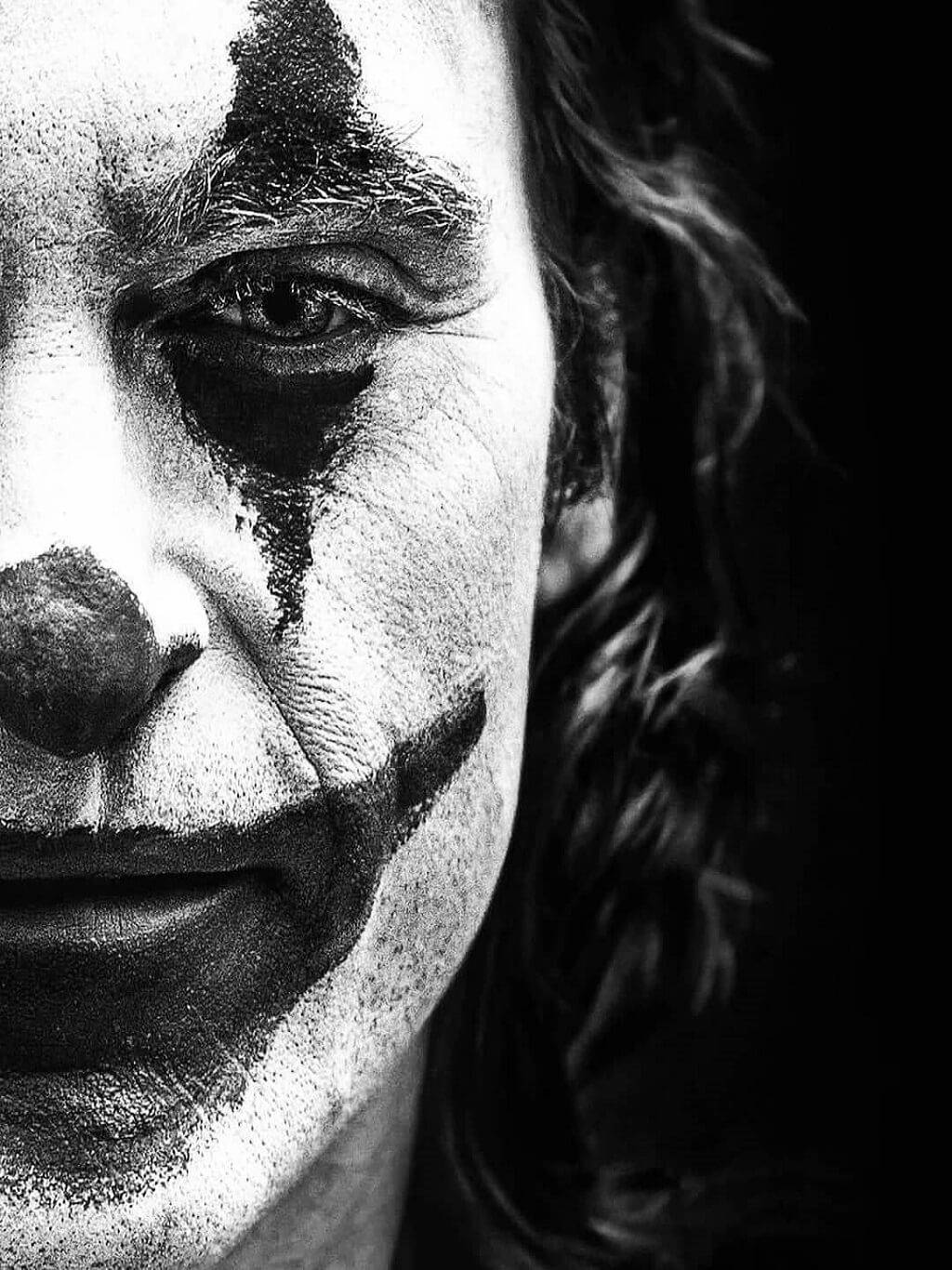 Black And White Joker 桌布 壁紙 — 一個令人毛骨悚然的黑白特寫，一個男人臉上塗抹著小丑妝容，眼神銳利，背景陰暗。