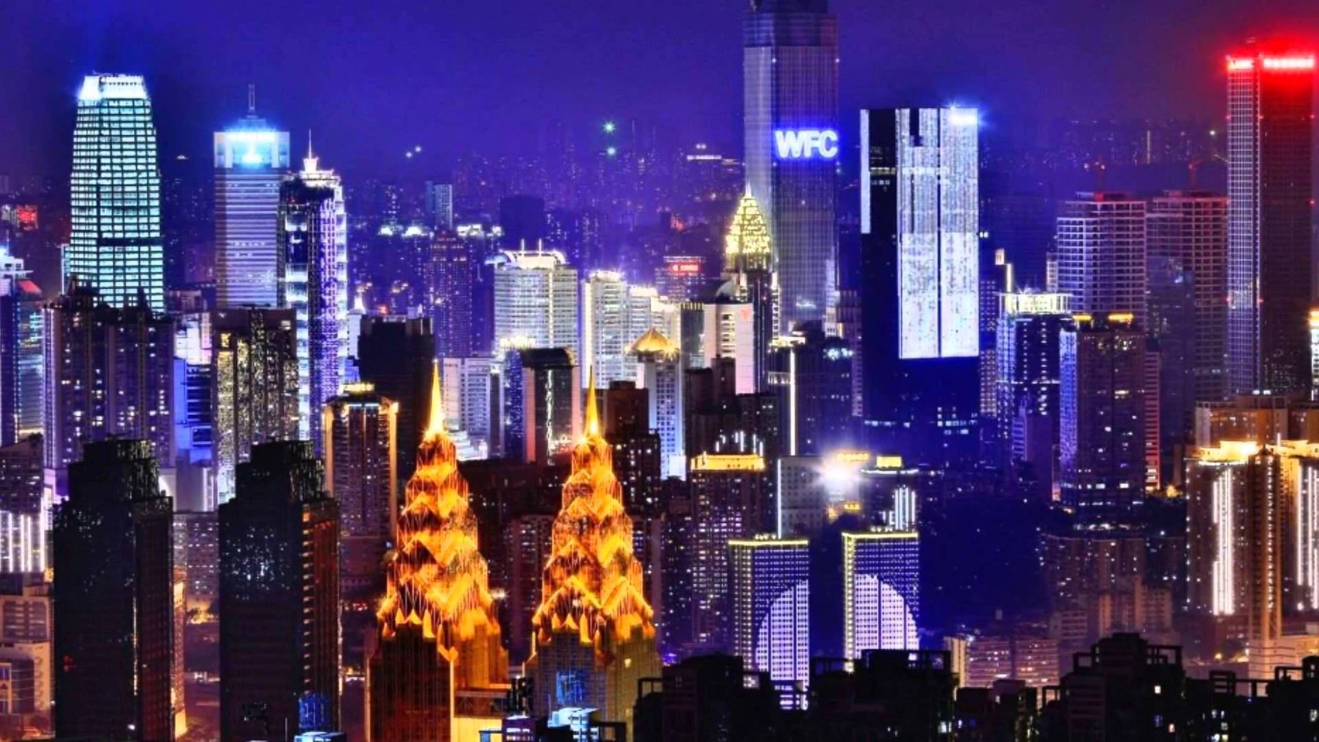 Chongqing 桌布 壁紙 — 一個令人眼花撩亂的夜景城市景觀，高聳的摩天大樓在黑暗的天空中閃爍著鮮豔的藍色、紫色和金色。