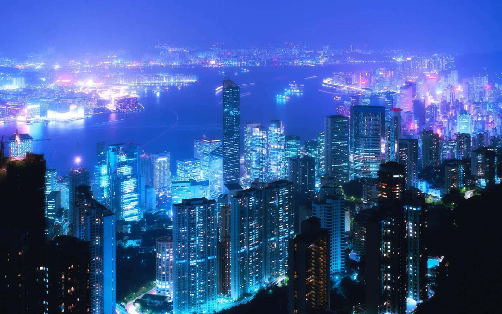 城市風景 桌布 壁紙 — 一個令人眼花撩亂的夜景城市景觀，高聳的摩天大樓沿著閃閃發光的水濱發出電藍色和紫色的光芒。