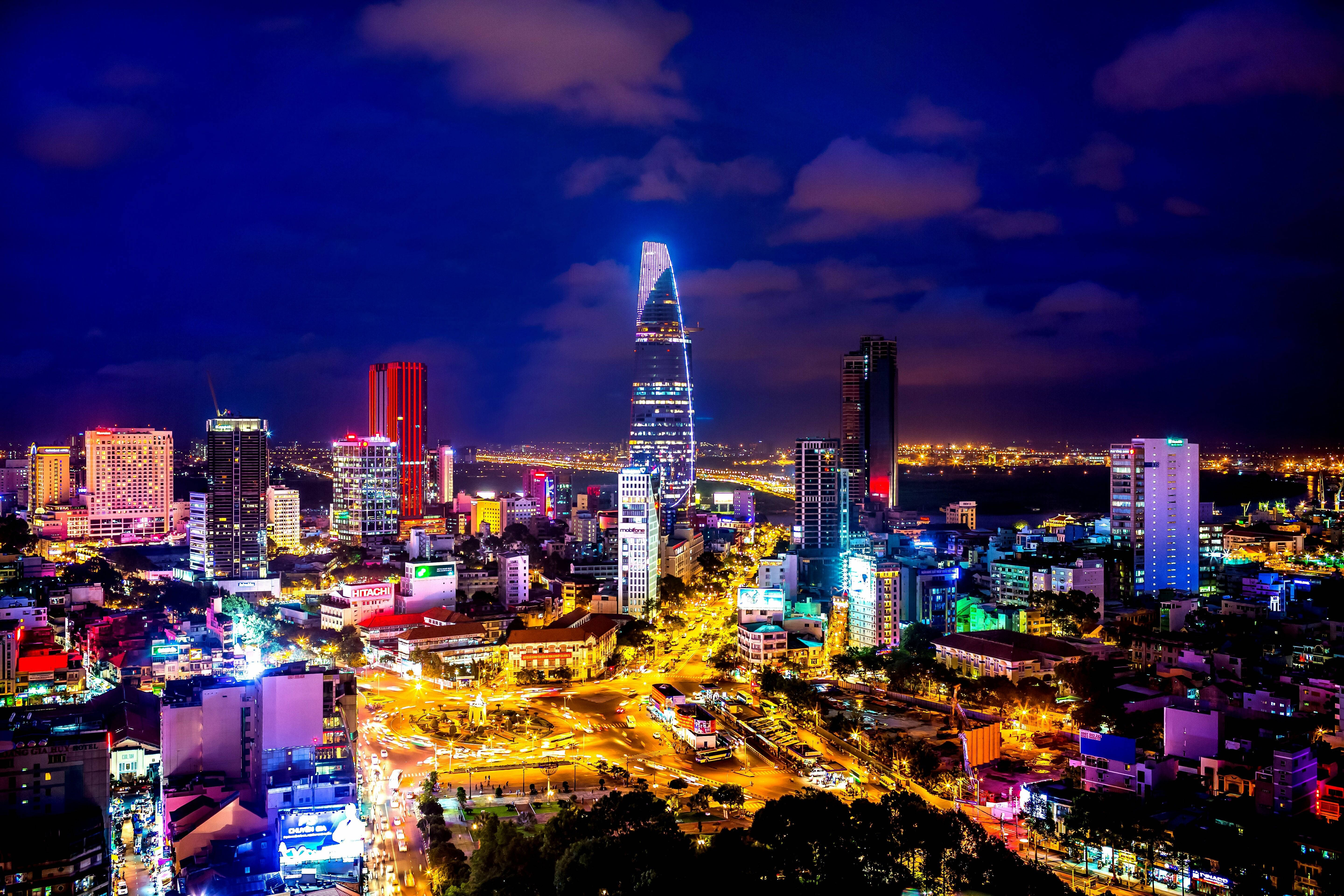 城市風景 桌布 壁紙 — 一個令人眼花撩亂的夜景城市景觀，霓虹燈閃爍的摩天大樓和發光的街道，在深藍色的天空下。