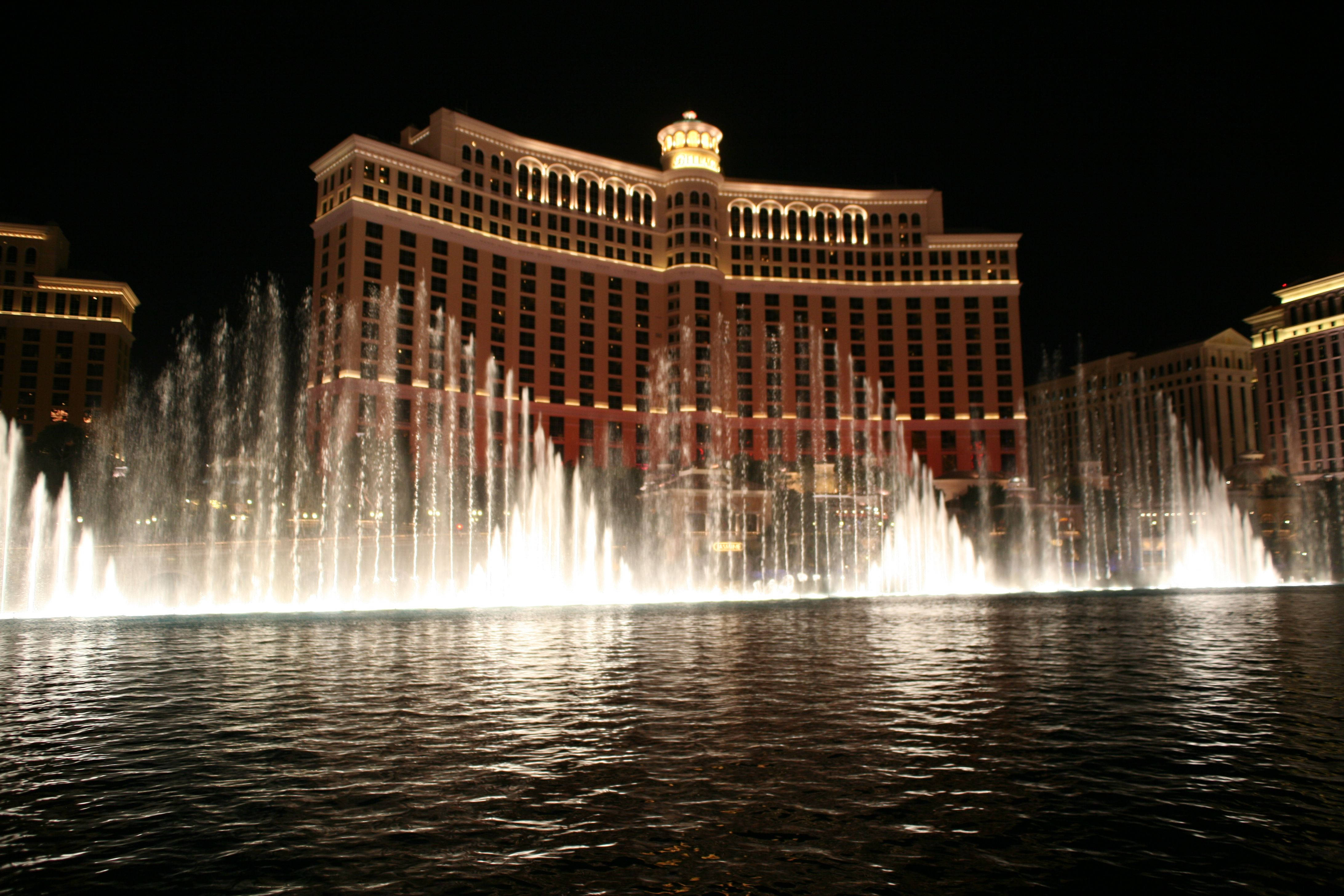 Las Vegas 桌布 壁紙 — 一個令人眼花撩亂的夜間噴泉表演在一個擁有拱形窗戶和金色燈光的宏偉照明飯店前爆發。