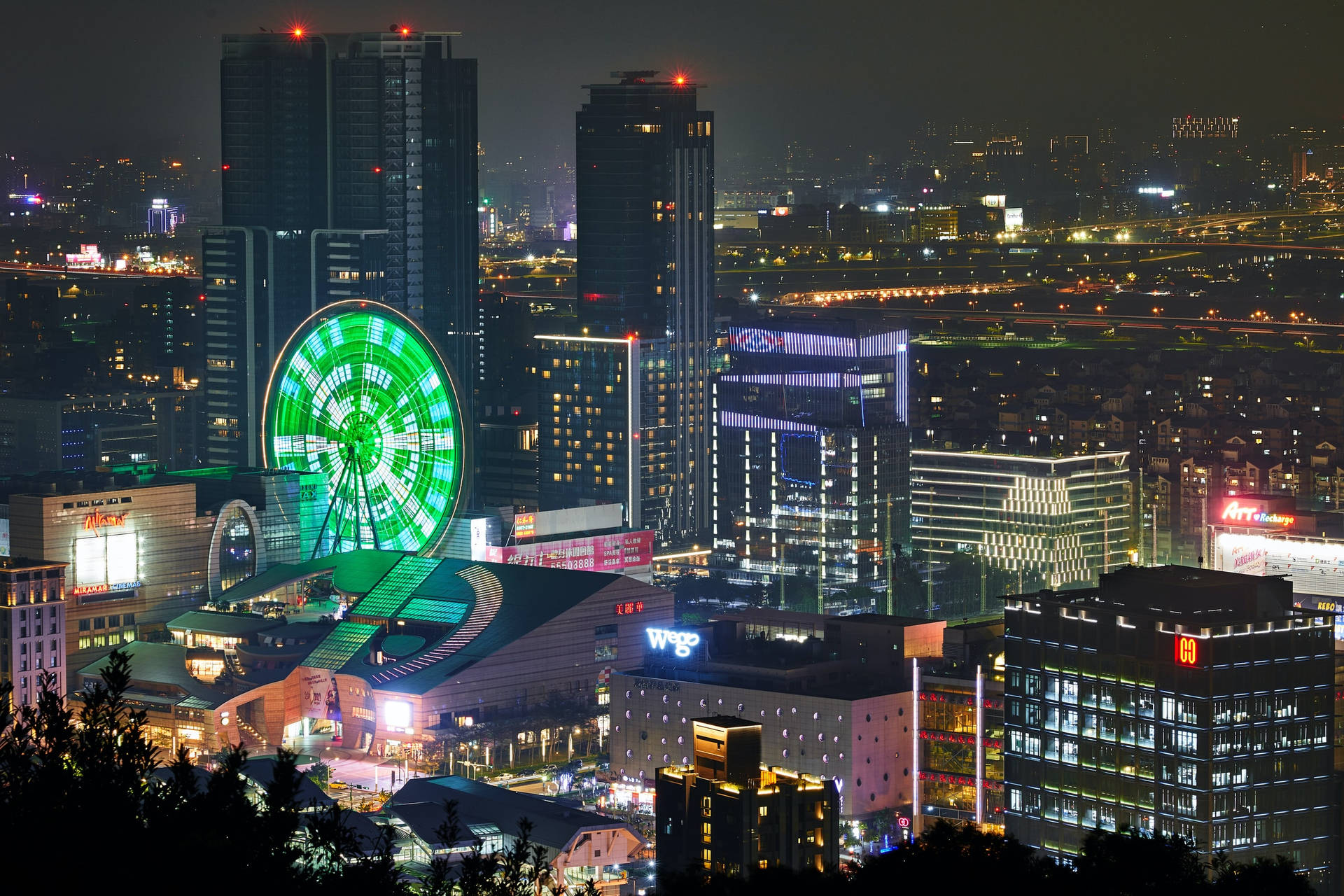 夜間燈火通明的城市天際線，帶有發光的綠色摩天輪。