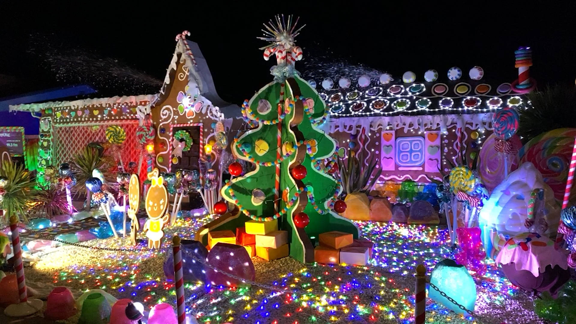 Gingerbread House 桌布 壁紙 — 一個令人眼花撩亂的夜間展示，超大型糖果主題結構閃爍著彩色燈光和裝飾。