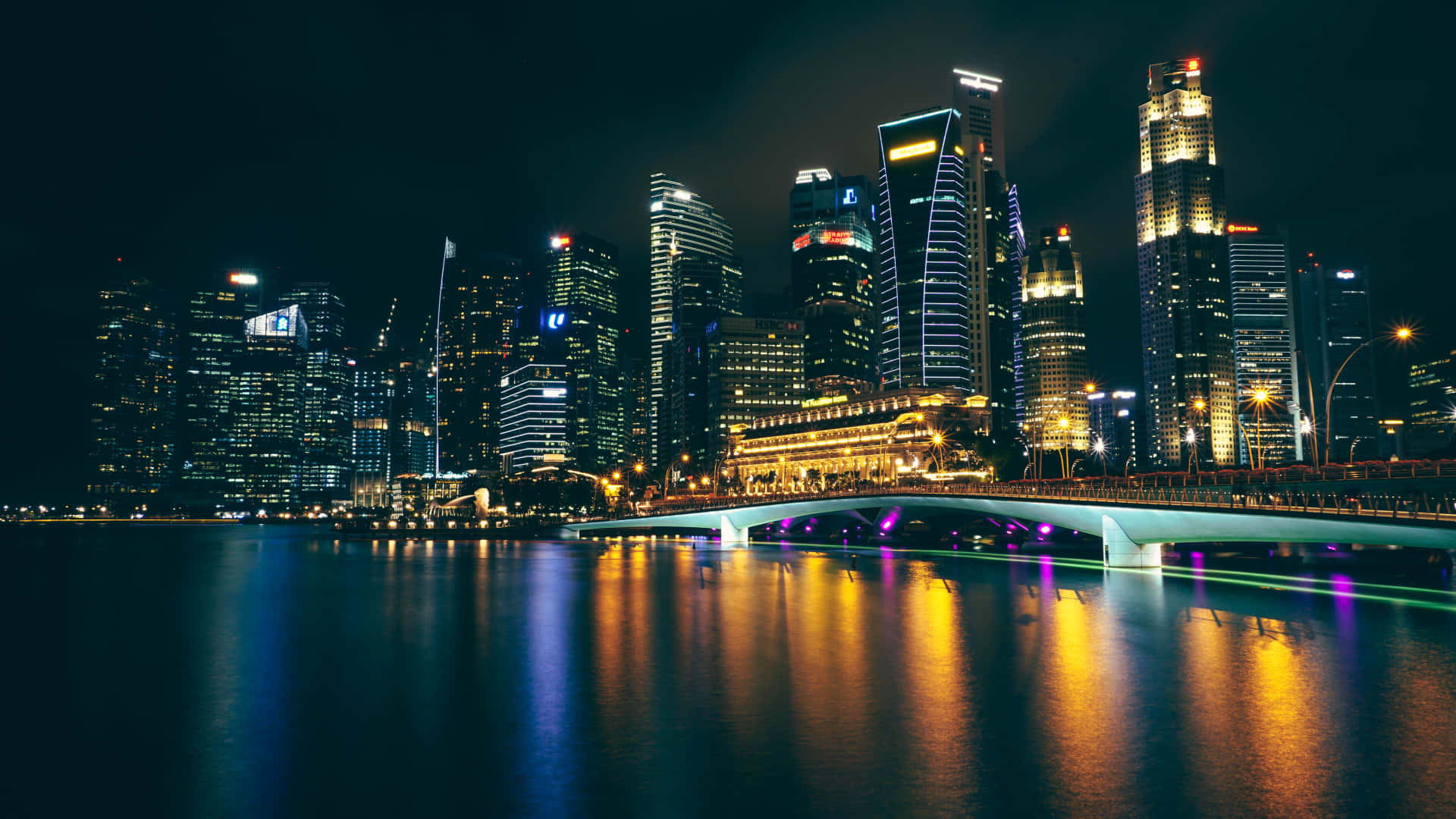 City Lights 桌布 壁紙 — 一個令人眼花繚亂的夜景城市景觀，有燈火通明的摩天大樓和一座發光的橋樑倒映在平靜的水面上。